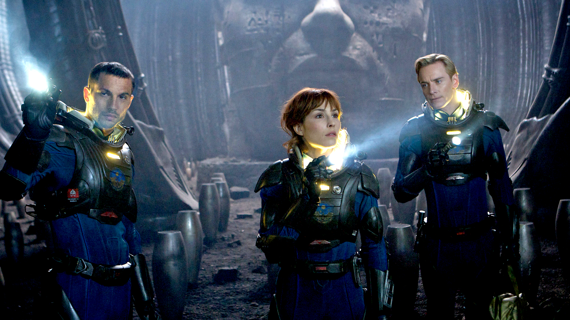 Meredith Vickers, David and Elizabeth Shaw from Prometheus in front of a patterned blue background.
