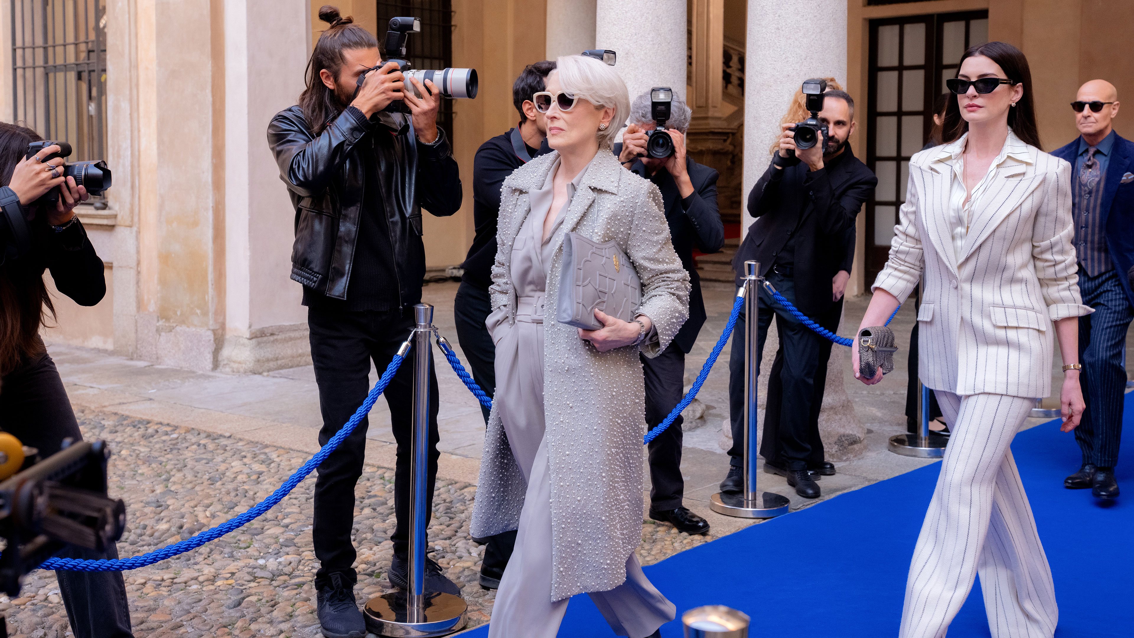 Miranda (Meryl Streep) and Andy (Anne Hathaway) walk down a blue carpet while paparazzi take photos of them in The Devil Wears Prada 2.