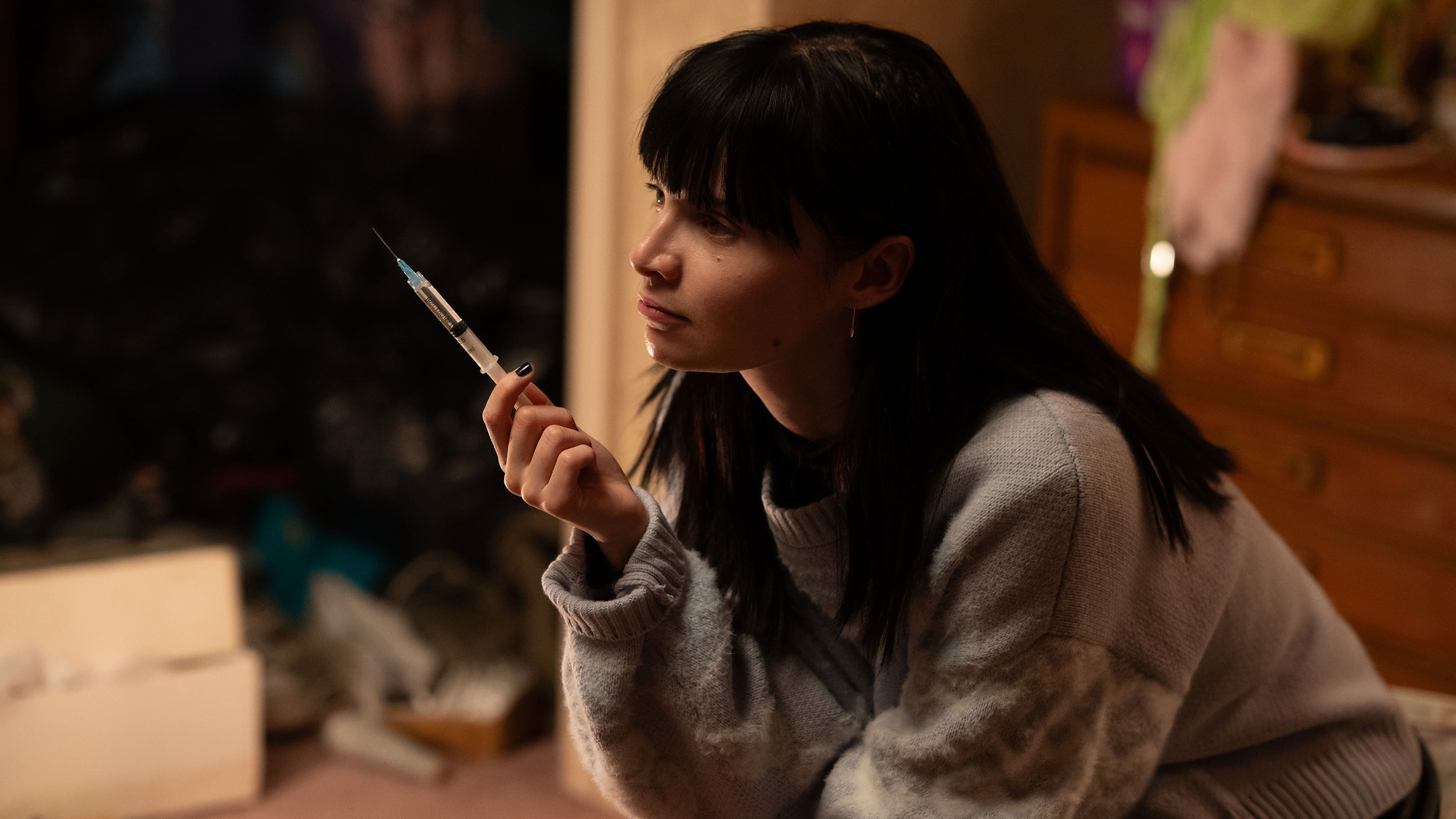 Catherine sits indoors holding a syringe.