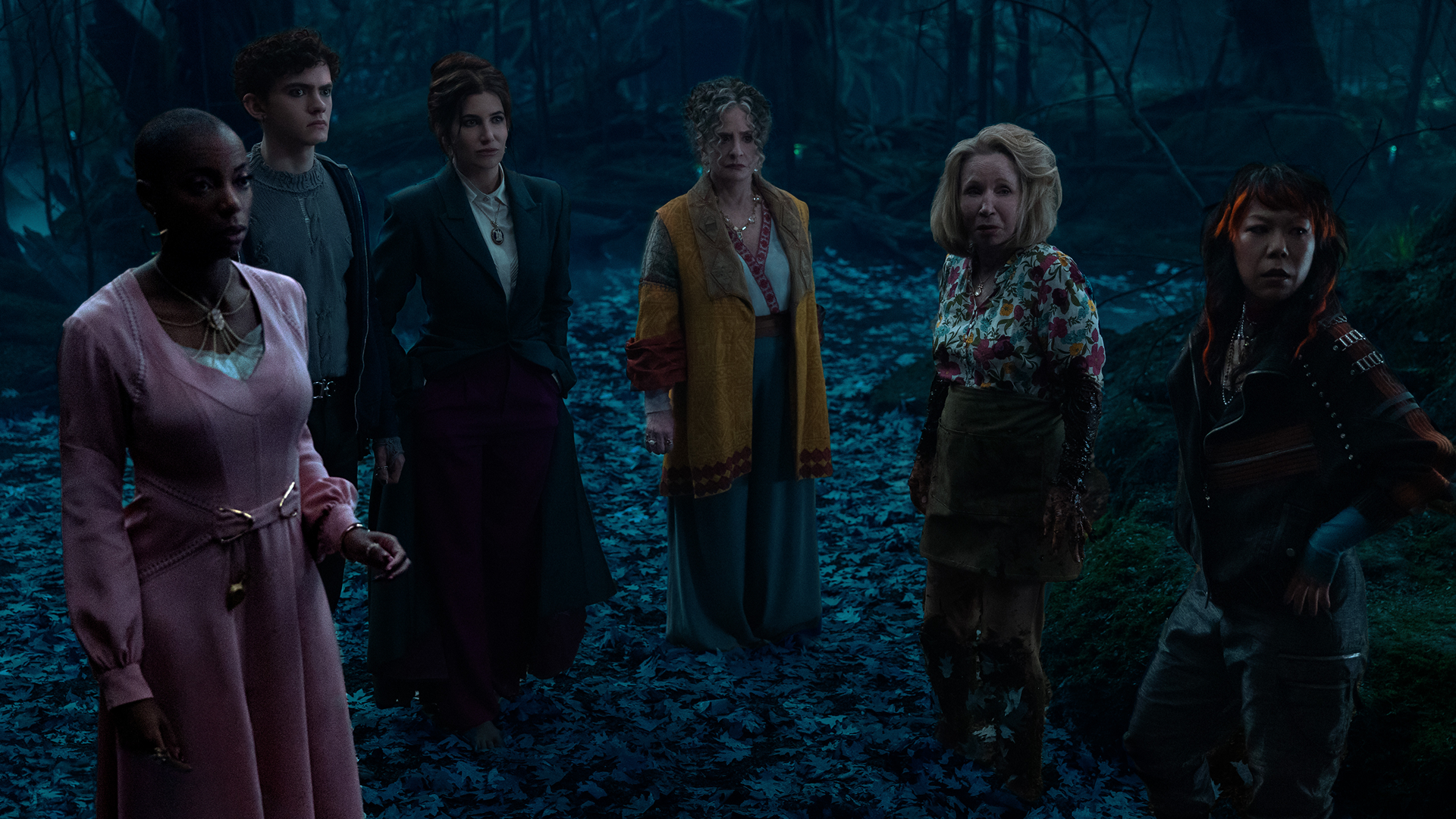 Agatha Harkness (Kathryn Hahn) and fellow characters gathered in a forest scene from Agatha All Along.