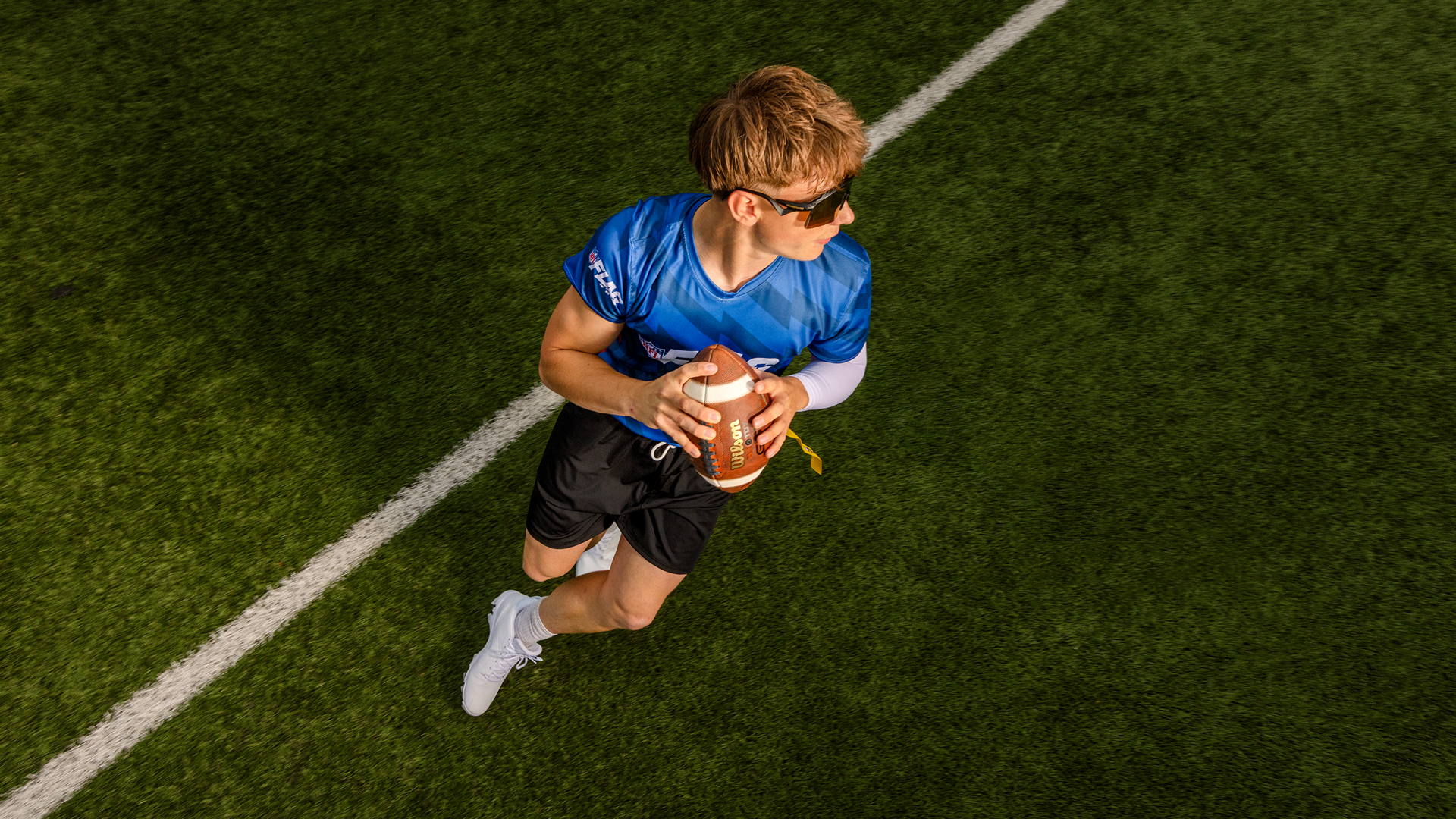 Overhead close-up of a young man running with the ball in a game of flag football.