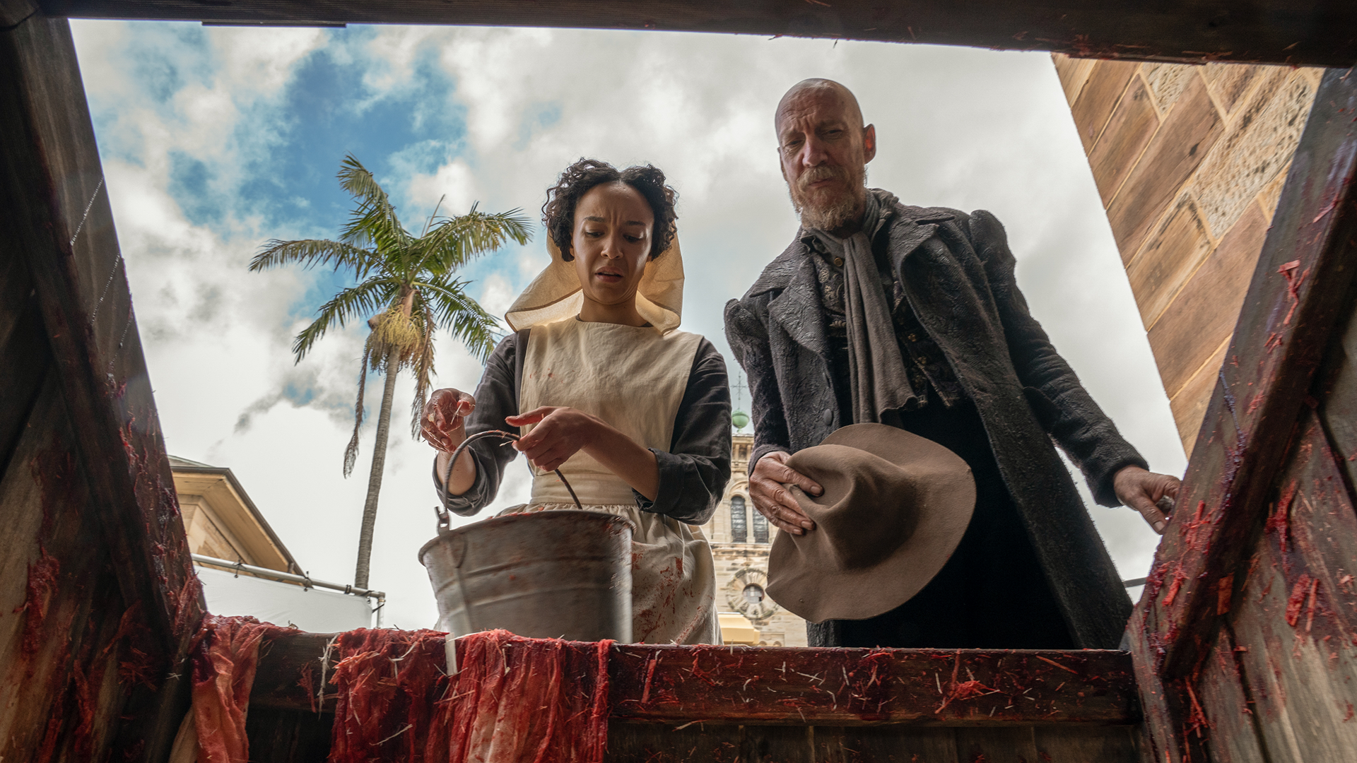 Marianne (Andrea Demetriades) and Fagin (David Thewlis) look down into a the opening of a blood-stained wooden pit