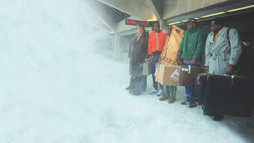 The Jamaican bobsled team in Cool Runnings standing outside an airport surrounded by snow, bundled up and holding their luggage.