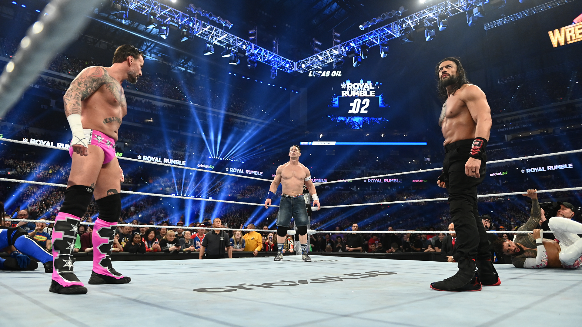 Wrestlers CM Punk, John Cena, and Roman Reigns standing in the ring at WWE Royal Rumble