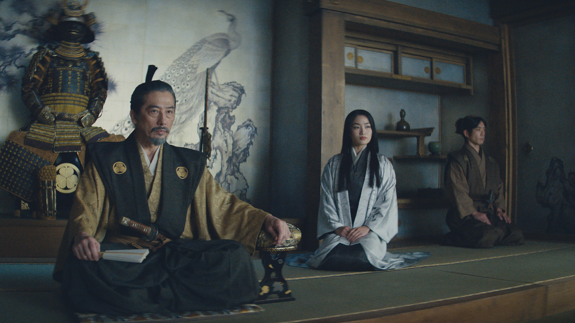 武将・吉井虎永（真田広之）が座っている。その隣に鞠子（アンナ・サワイ）が座っている。