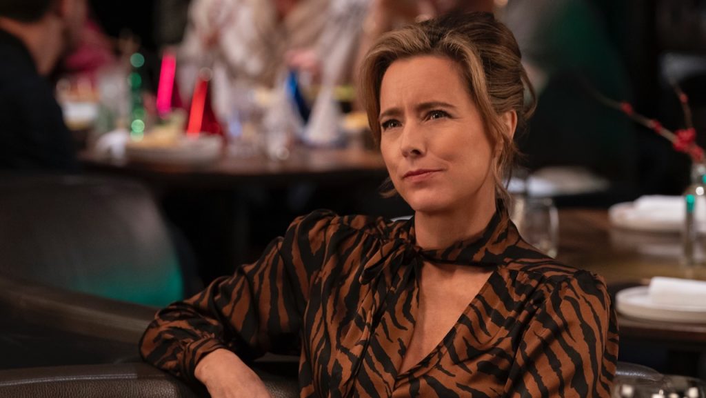 Téa Leoni sits in a restaurant wearing a brown and black patterned blouse.