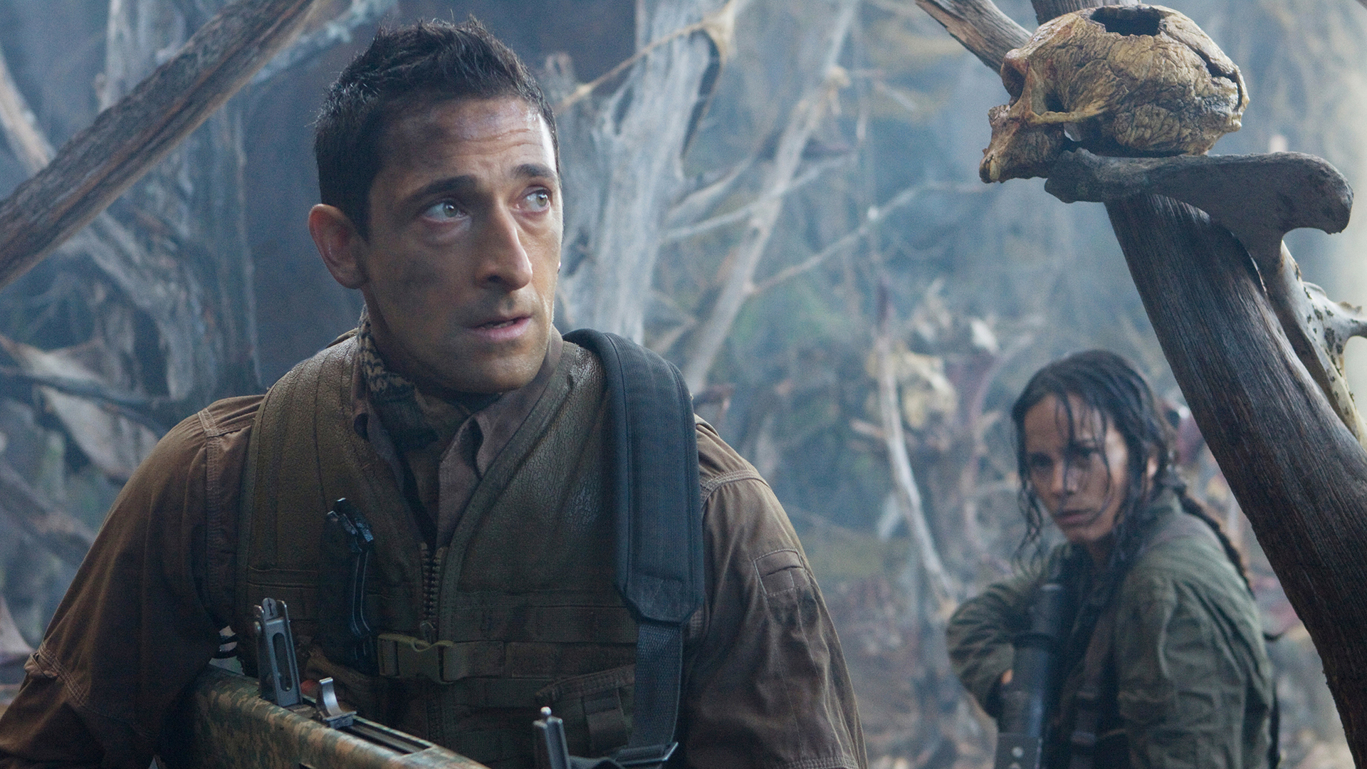 Royce (Adrien Brody) e Isabelle (Alice Braga) observan con cautela en torno a un bosque neblinoso