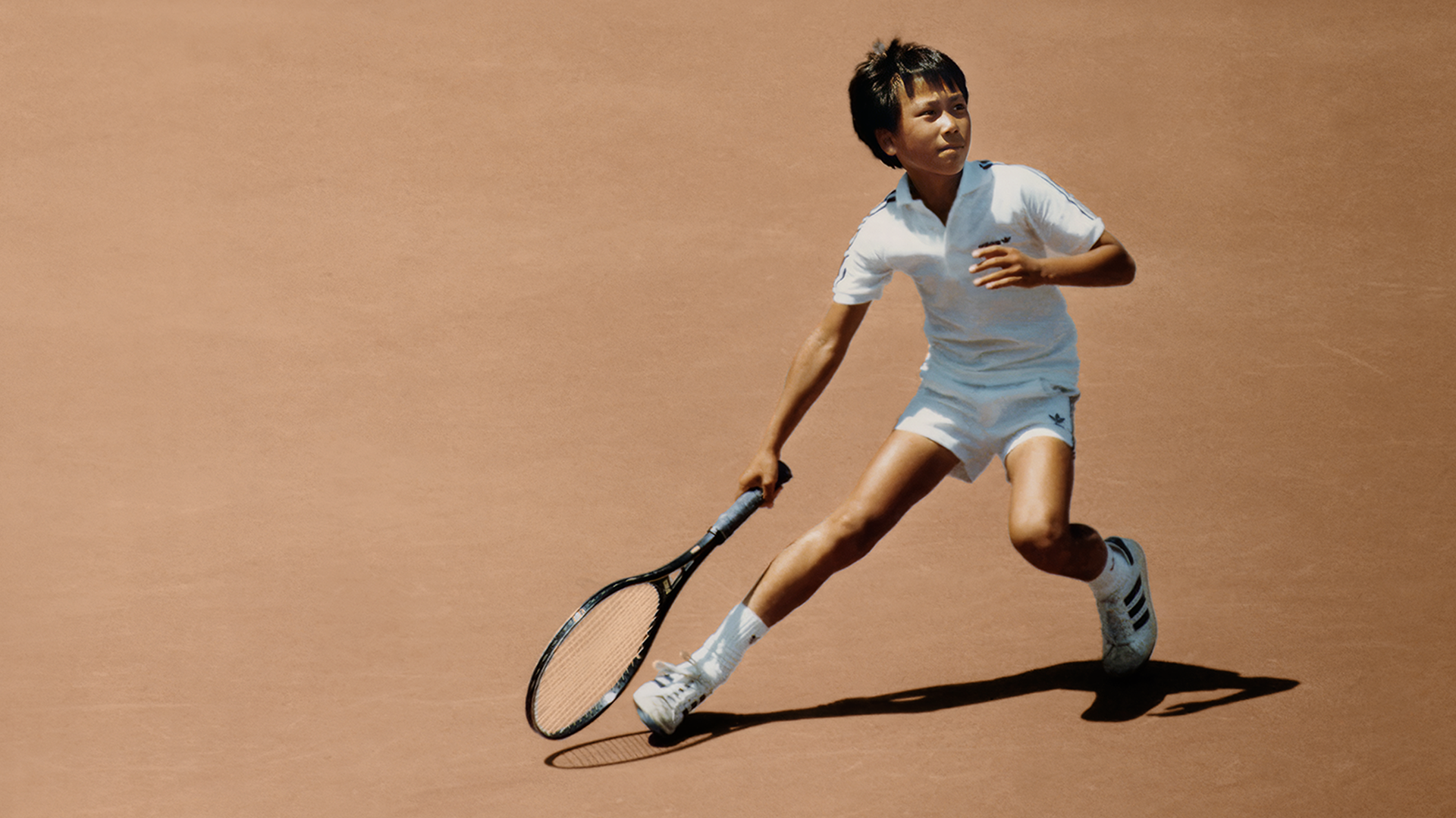 A young Michael Chang plays on a clay court.