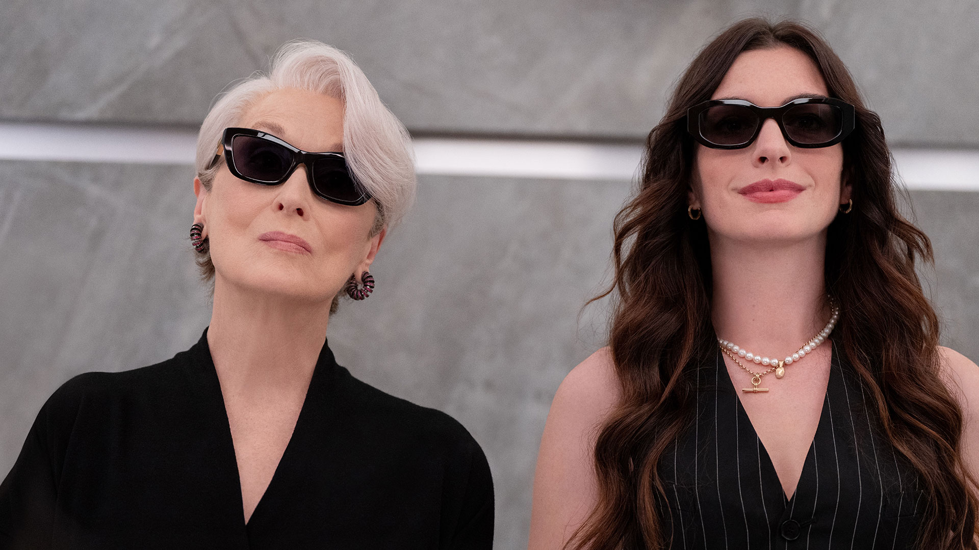 Key art for The Devil Wears Prada 2 featuring Miranda Priestly and Andy Sachs fashionably dressed wearing dark sunglasses against a minimalist grey backdrop.