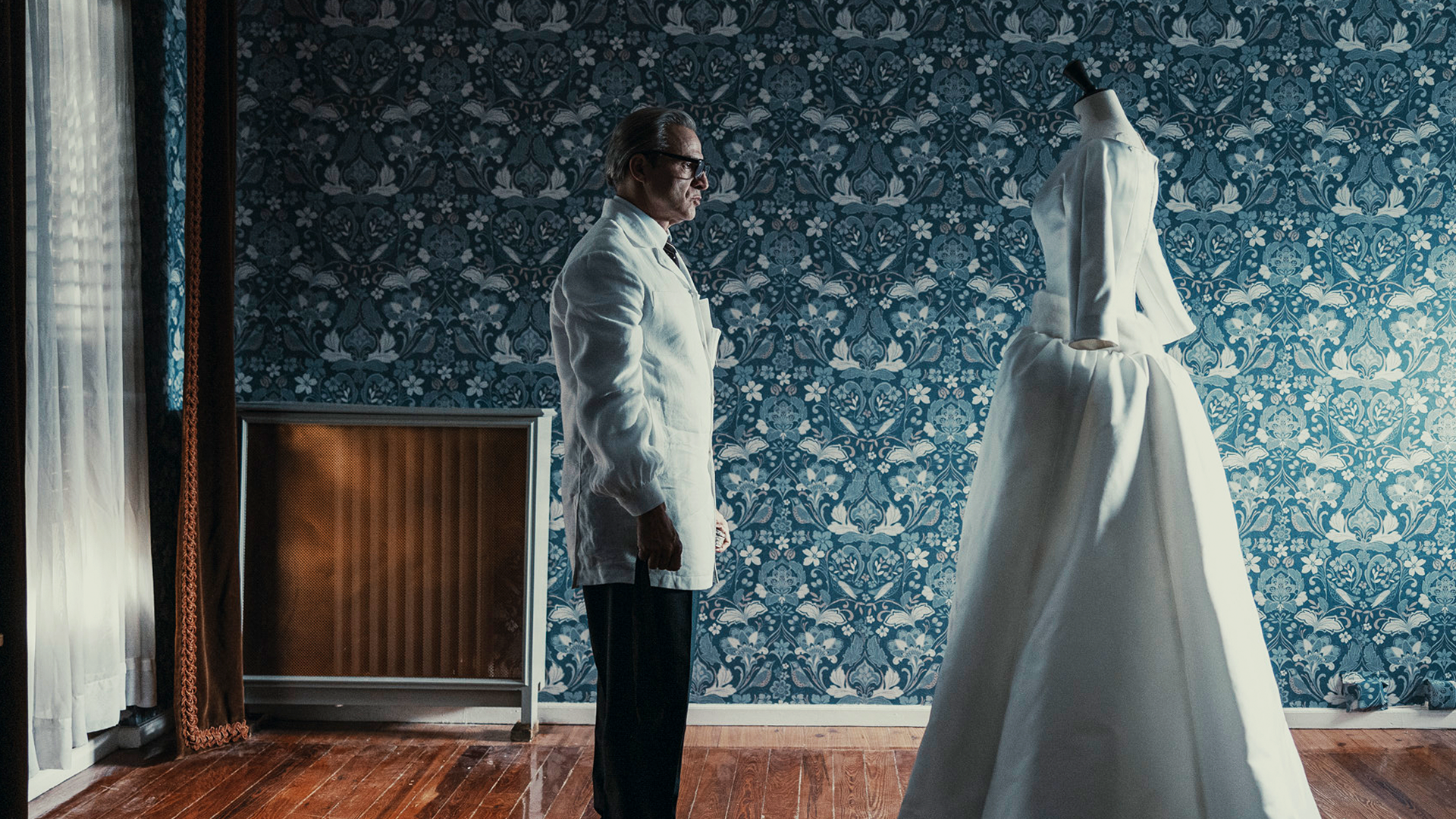 Cristóbal Balenciaga (Alberto San Juan) looks over a long white dress on a mannequin.