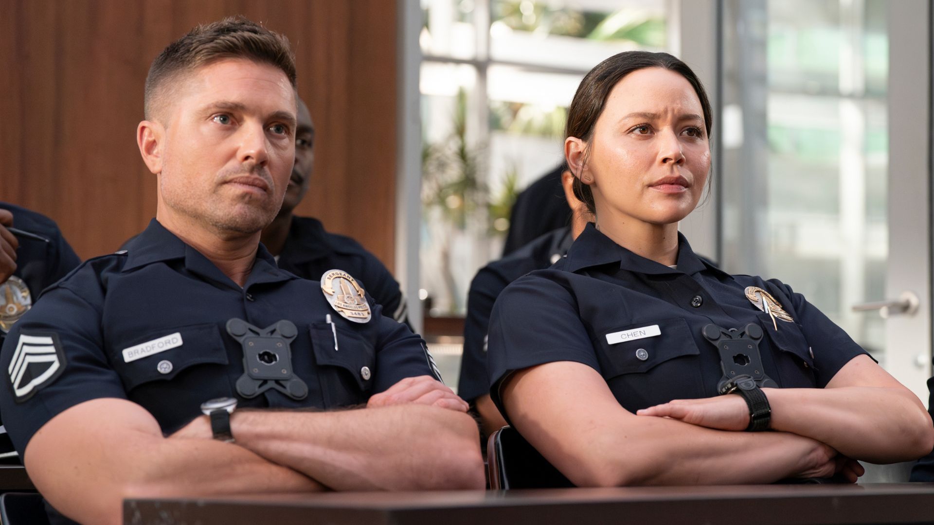 Sergeant Bradford and Officer Chen sit with arms crossed, listening intently in a scene from The Rookie.