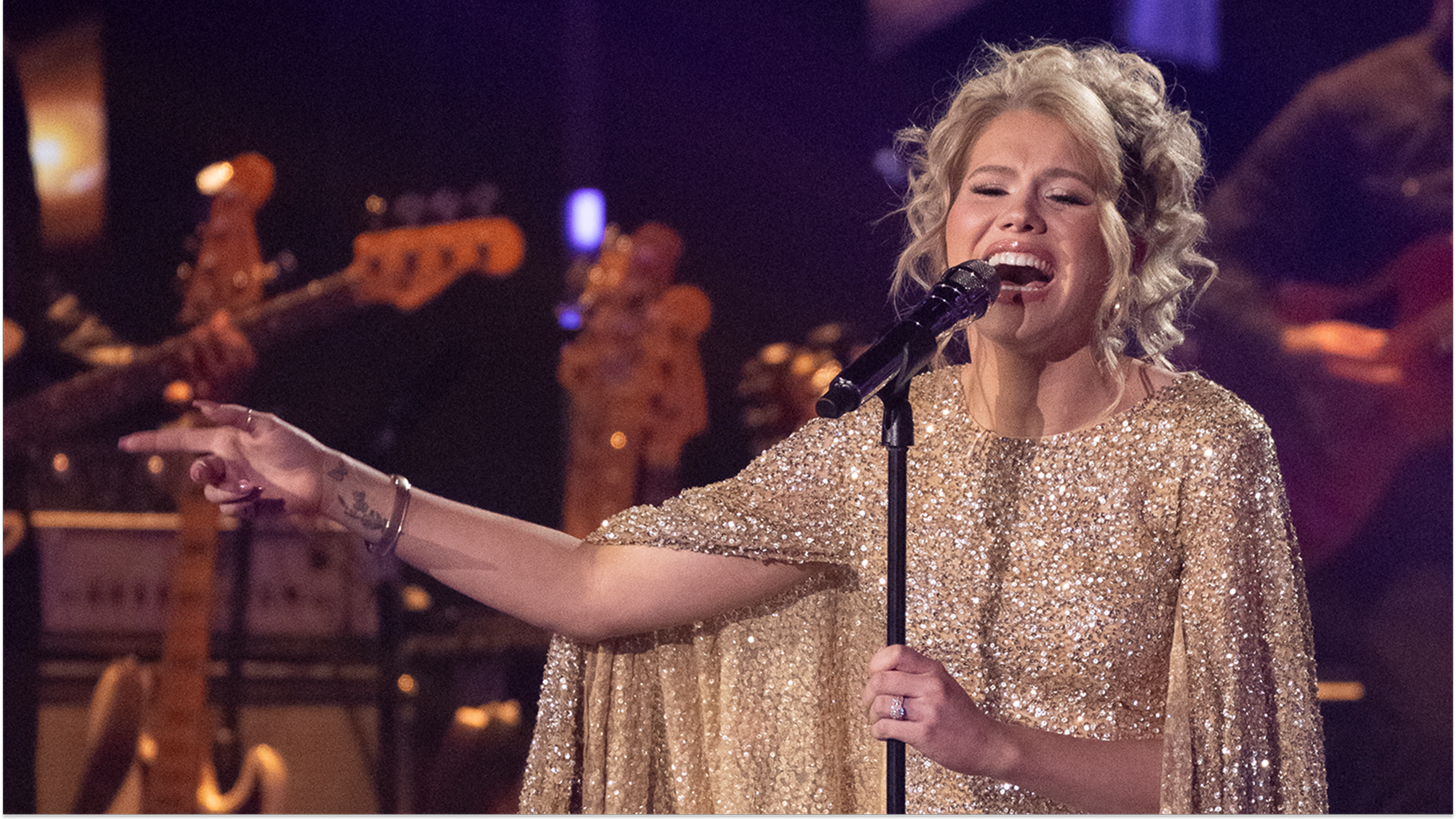 Closeup of American Idol finalist Hannah Harper singing on stage, in a sequinned gold dress with a cape