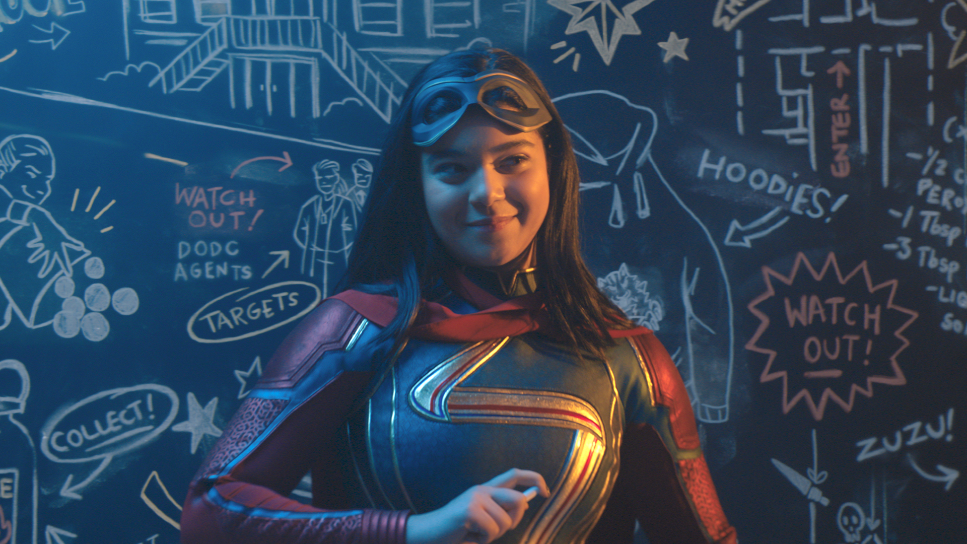 Ms Marvel smiles in front of a doodled blackboard