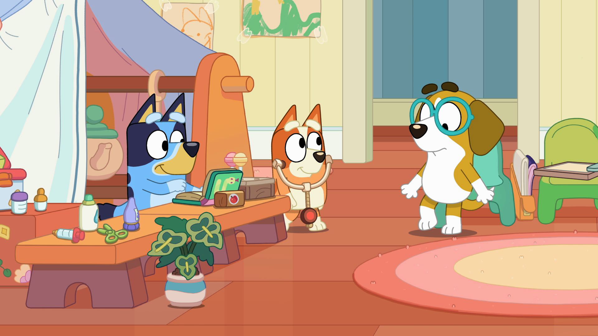 A colorful scene from the animated children's show Bluey, featuring Bluey sitting behind a wooden toy counter typing on a green laptop while Bingo wears a toy stethoscope, both looking toward their brown dog friend wearing large blue glasses.