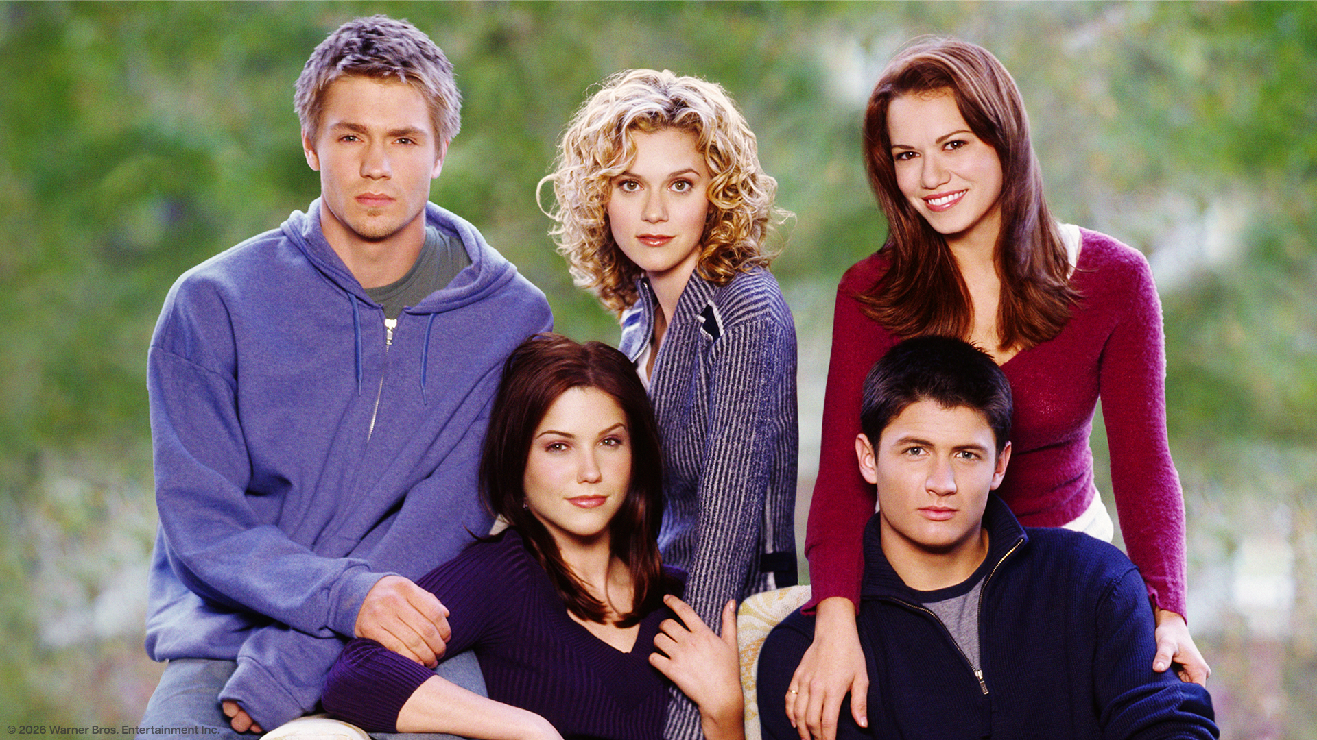 A promotional group photo of the core cast from the television series One Tree Hill posing outdoors against a blurry green background. 