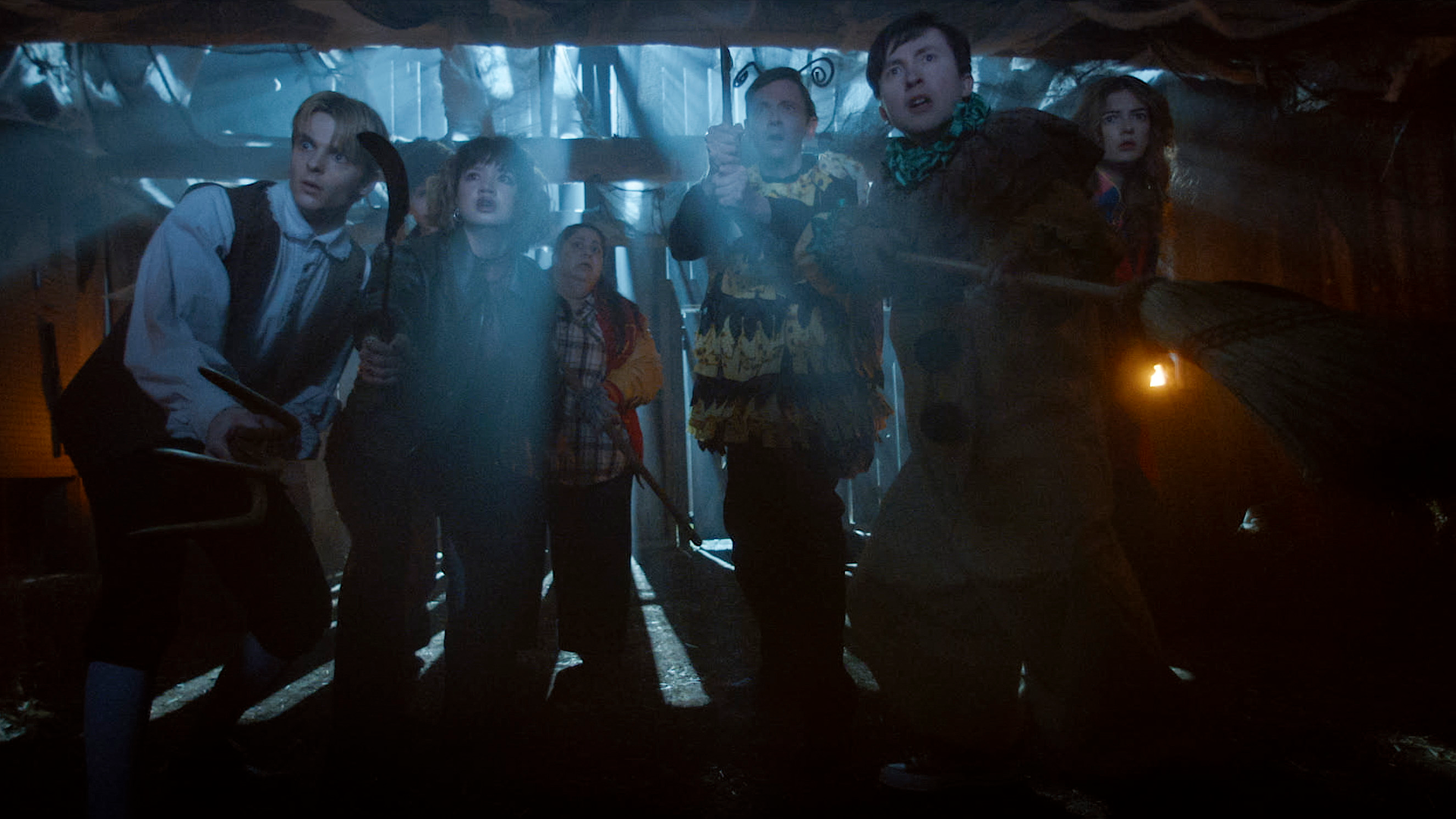 A group of friends, including Will (Ethan Herisse), Lisa (Chloe Caro), and Sarah (Madison Ekstrand), look up in fear and confusion within a dimly lit barn in Carved.