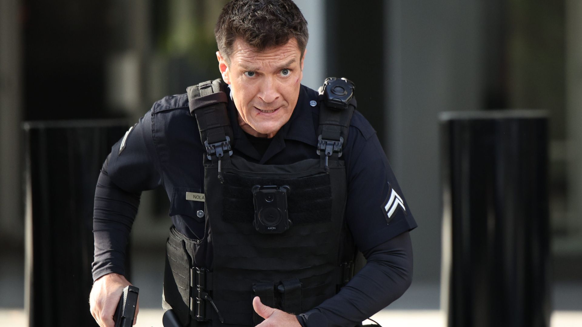Officer Nolan, played by Nathan Fillion, moves in tactical gear with gun drawn in a tense scene from The Rookie.