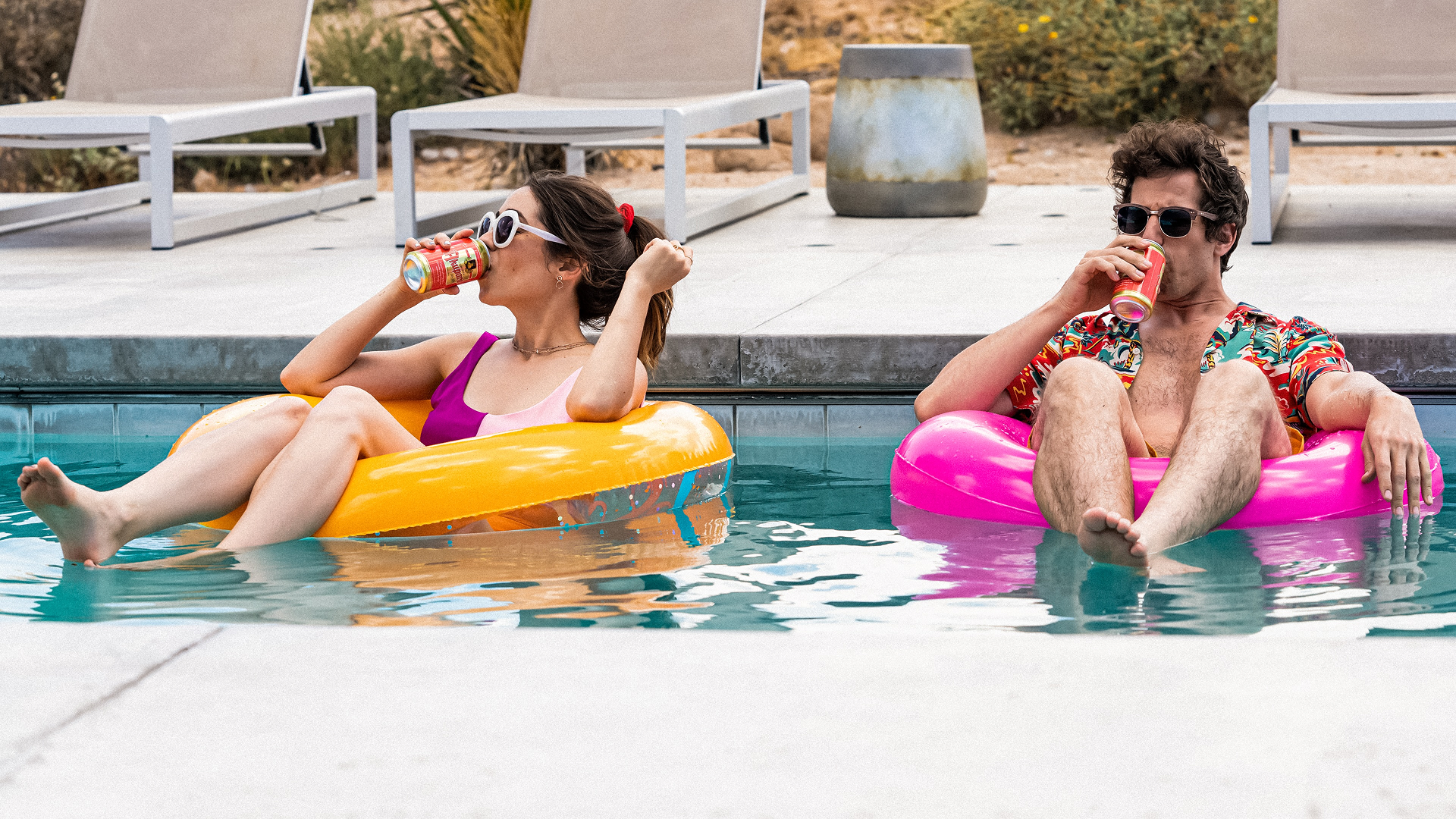 Sarah (Cristin Milioti) and Nyles (Andy Samberg) sit on inflatable rings in a pool while drinking from cans