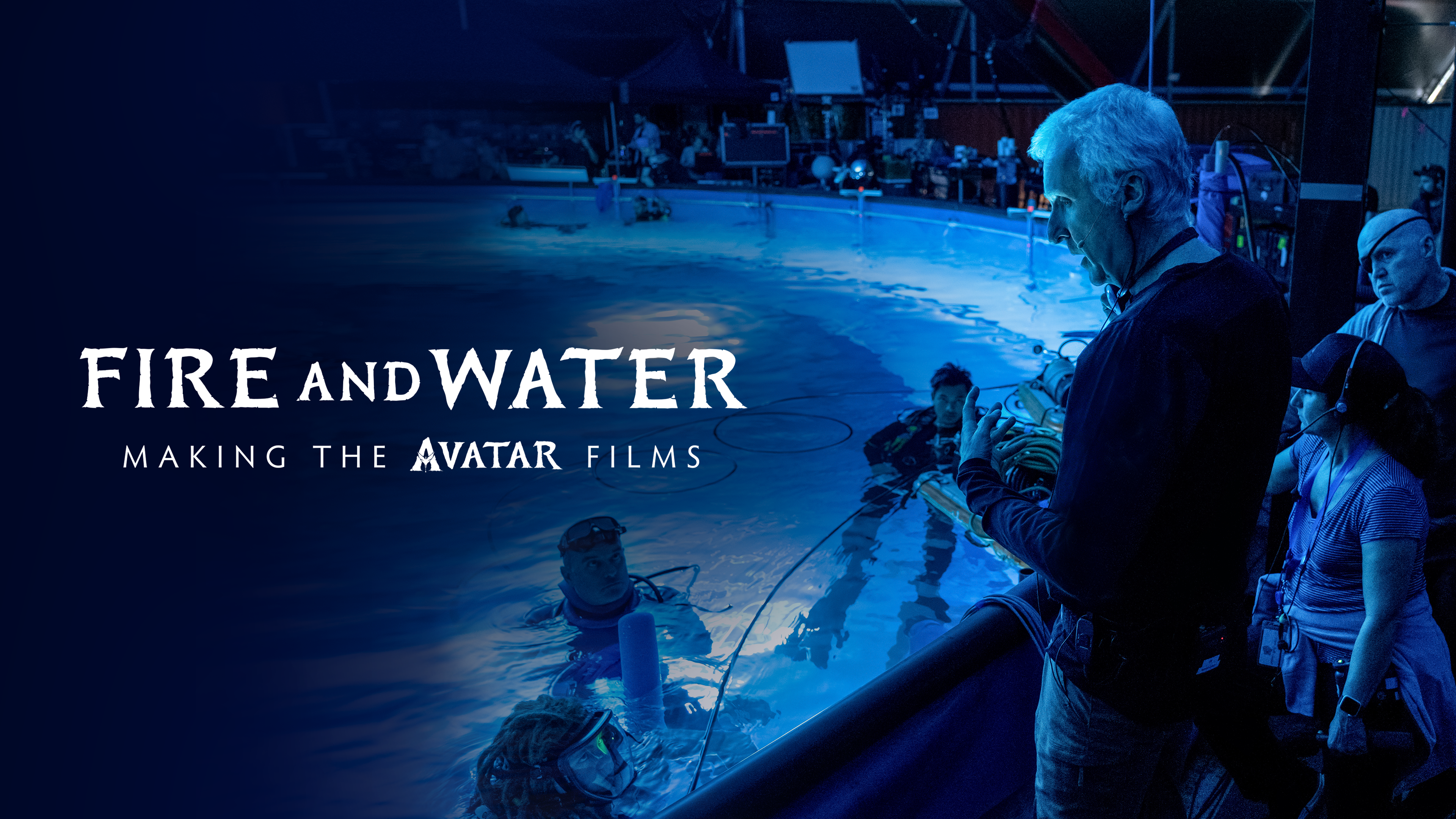 James Cameron is seen from behind, giving direction to a group of performers in high-tech gear in a swimming pool