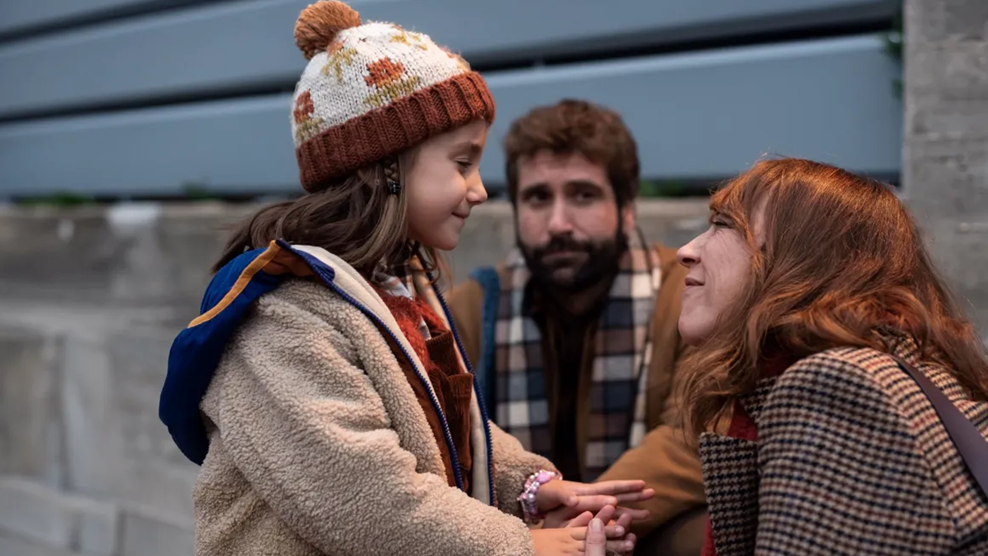 Cris (Lorena López) crouches down and smiles at her daughter Cloe, with Cloe's father Diego (Ricard Farré) watching them.