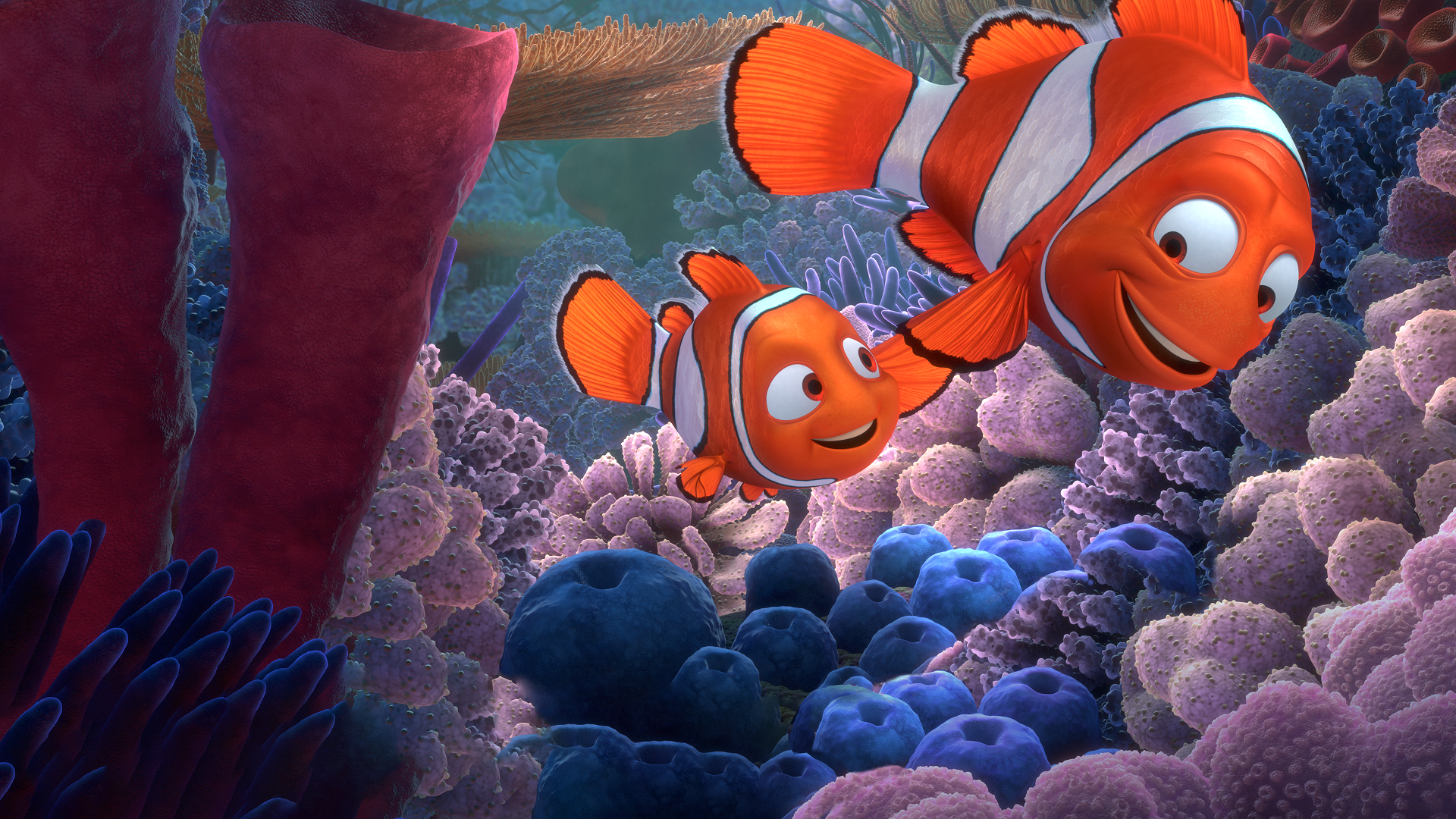 An animated underwater scene from Finding Nemo shows Nemo (Alexander Gould) swimming happily next to his father, Marlin (Albert Brooks), amidst a vibrant coral reef filled with purple, blue, and orange sea anemones.
