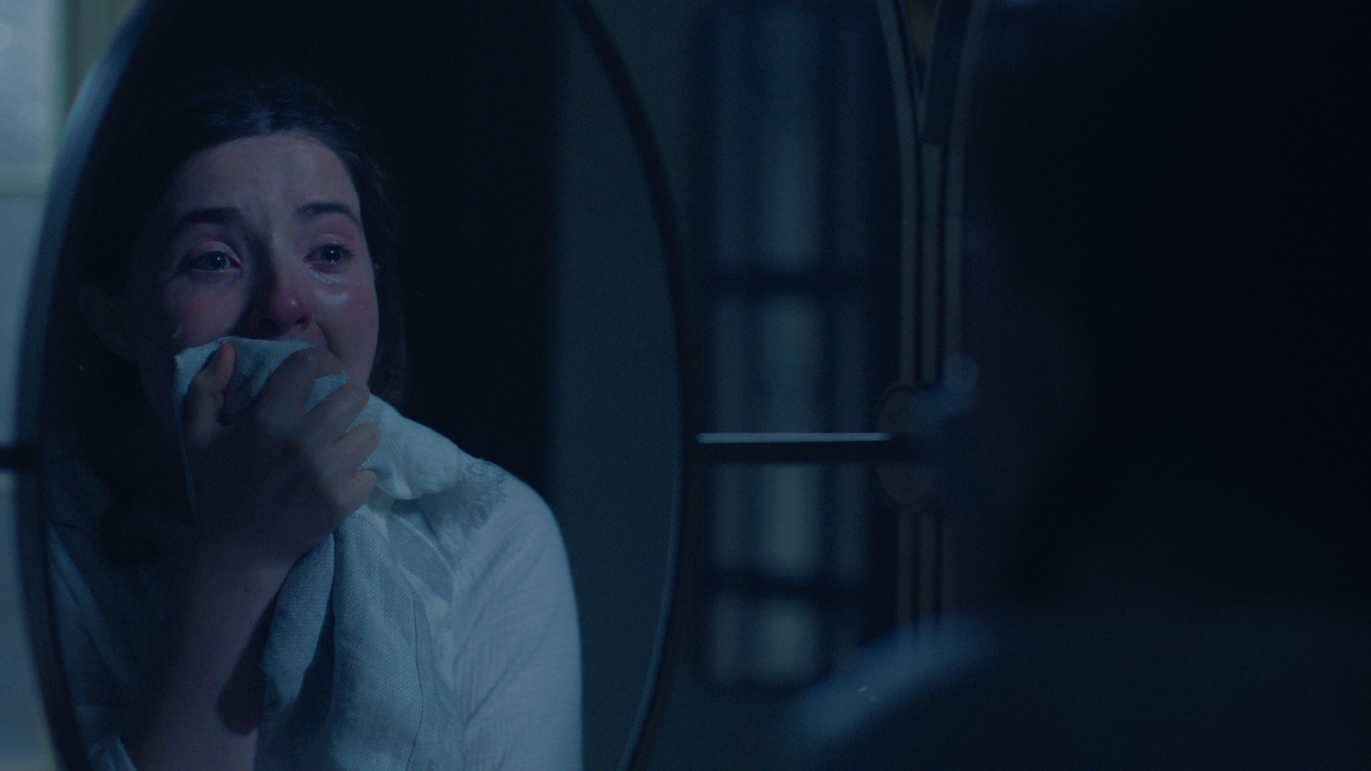 Lucy Halliday as the character Daisy looking shocked in a mirror in The Testaments