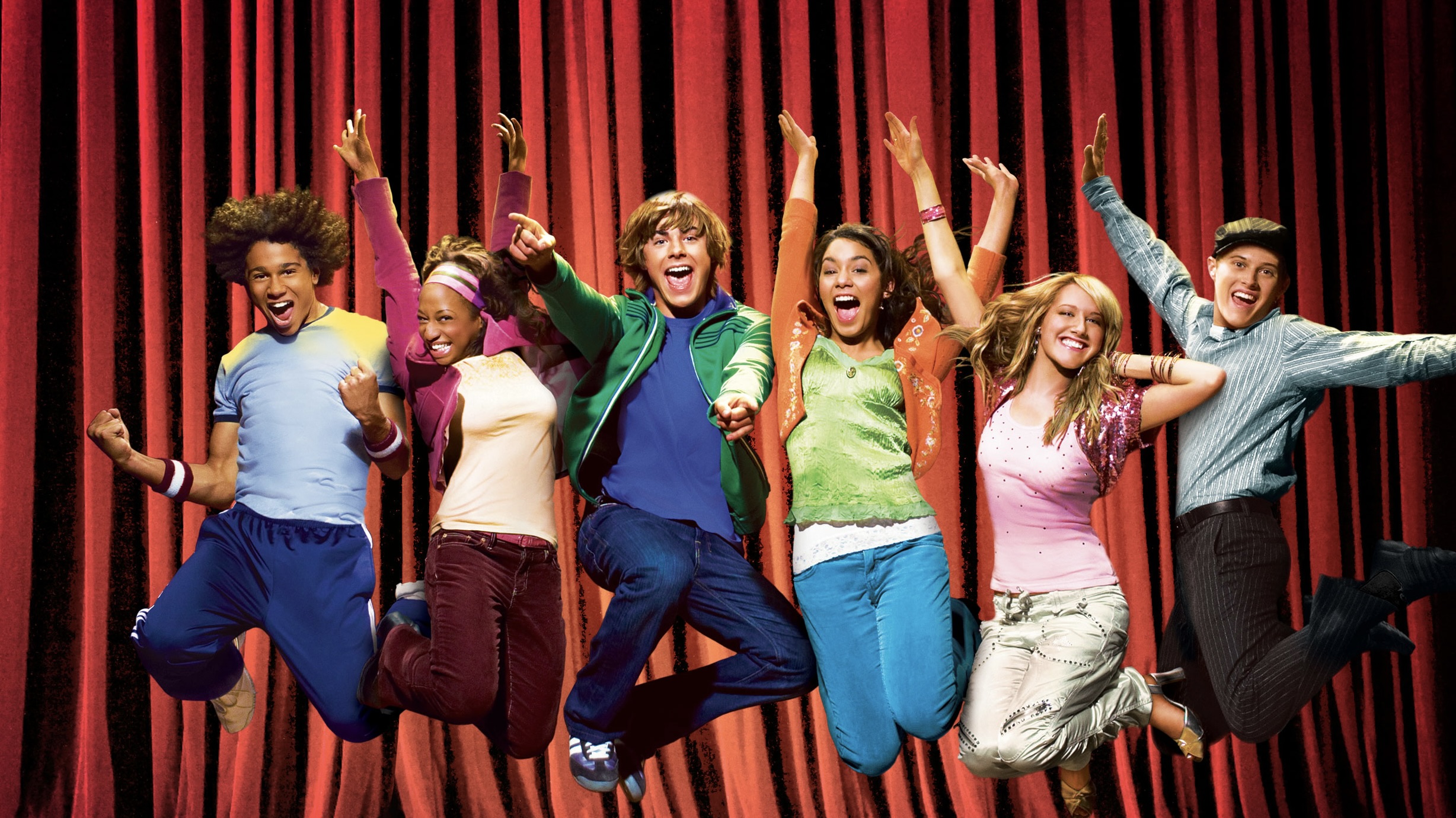 The cast of Disney’s High School Musical jumping in the air in front of a red theater curtain.