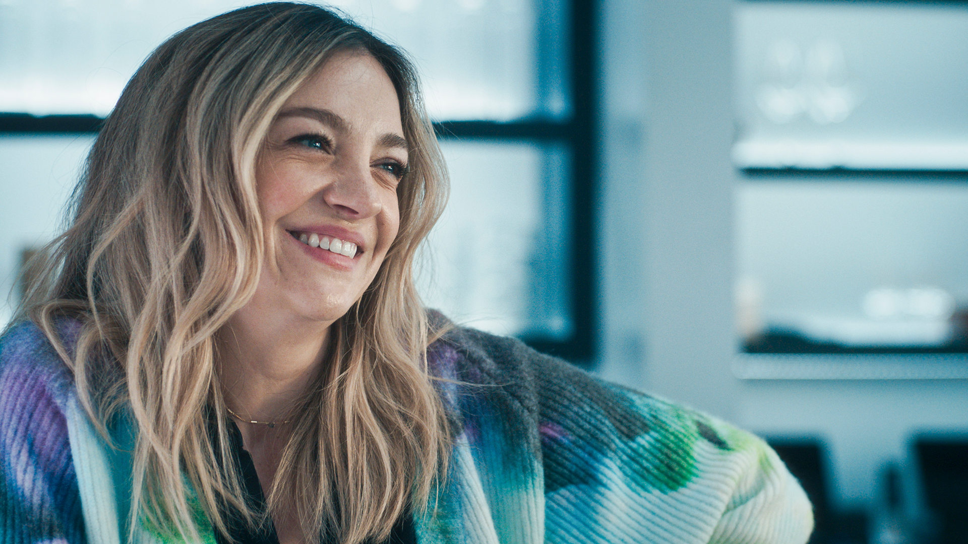 A close-up shot captures Natalie "Sugar" Berzatto (Abby Elliott) smiling warmly while looking off-camera, dressed in a vibrant tie-dye print V-neck cardigan.