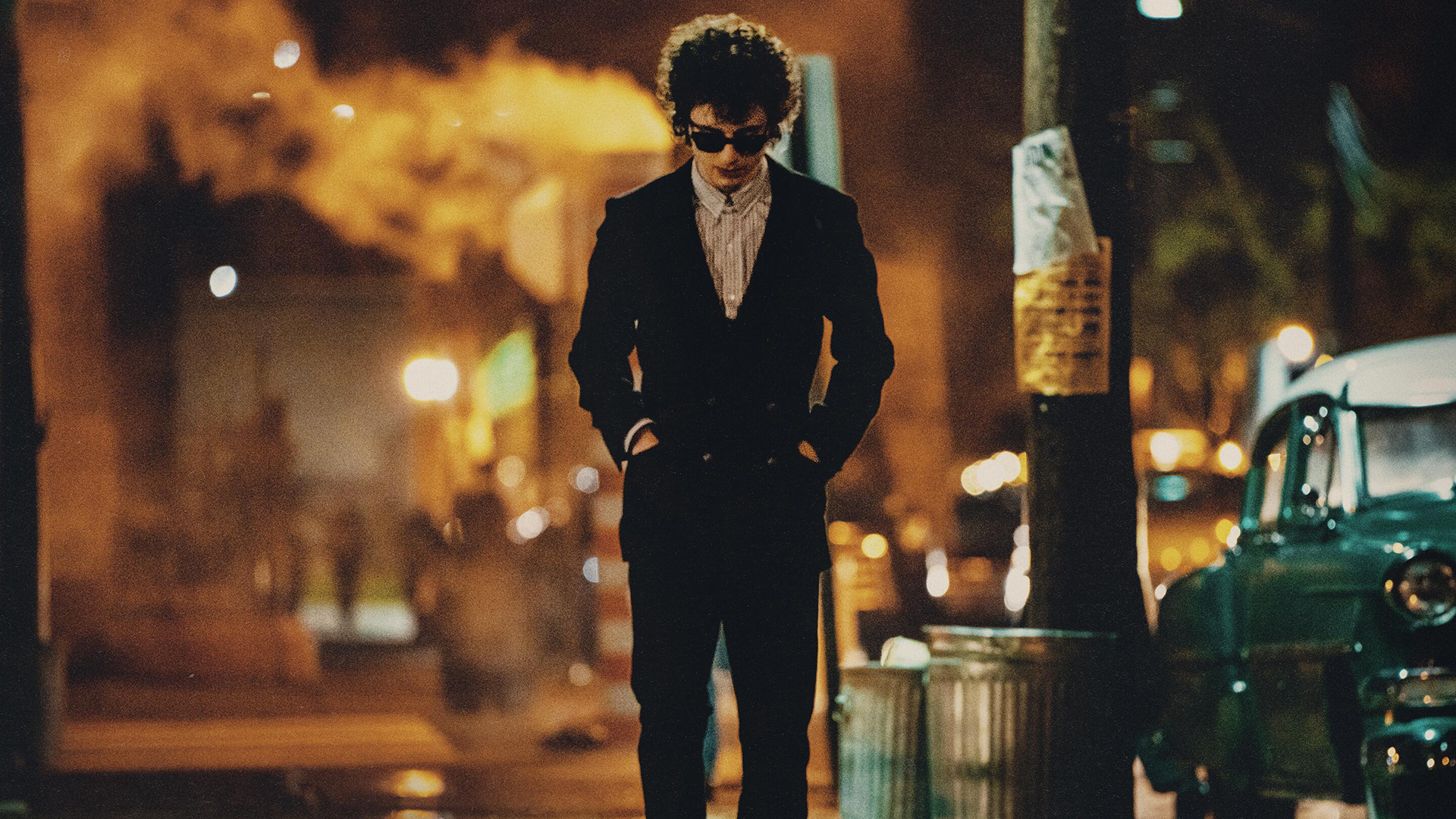 Bob Dylan (Timothy Chalamet) walking down a street with his hands in his pocket and looking at the ground.