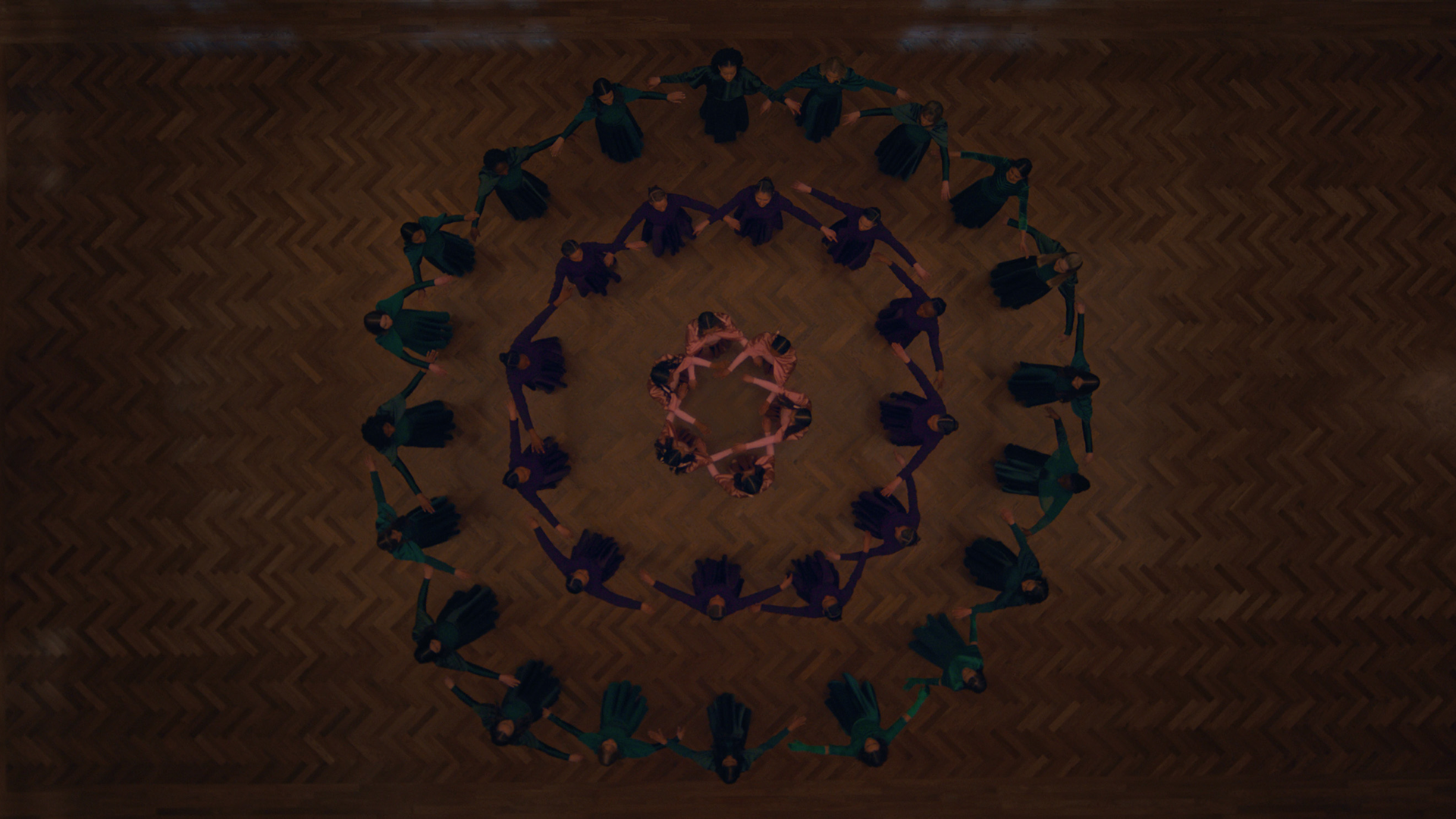 A birds eye view of a large group of people making shapes by holding hands in the circle in The Testaments