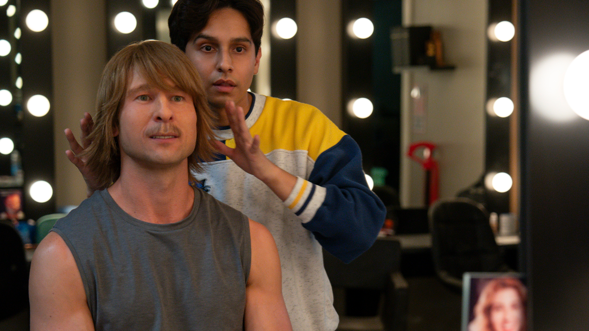 Russ Holliday (Glen Powell) in chair and makeup transforms into his Chad Powers persona with Danny's help (Frankie Rodriguez).
