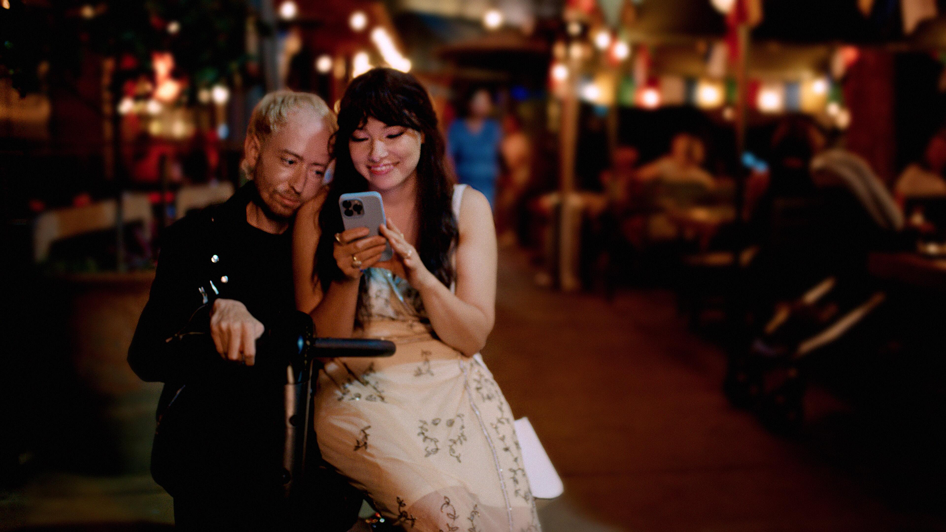 Madi (Jessica Parker Kennedy) and Danny (Danny Kurtzman) sit together on a mobility scooter looking at Madi's phone
