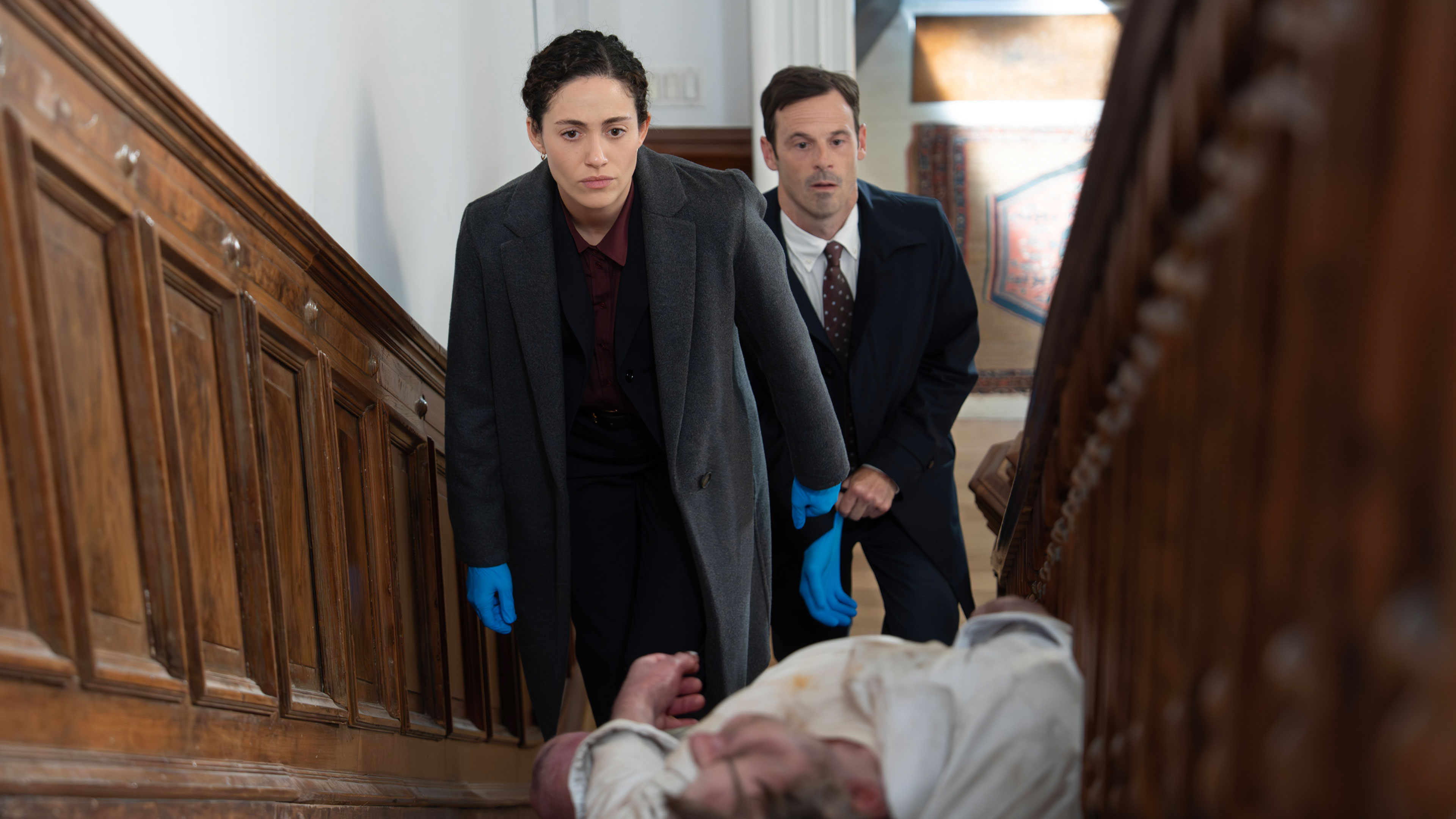 Alice and Danny examine a body on a staircase.