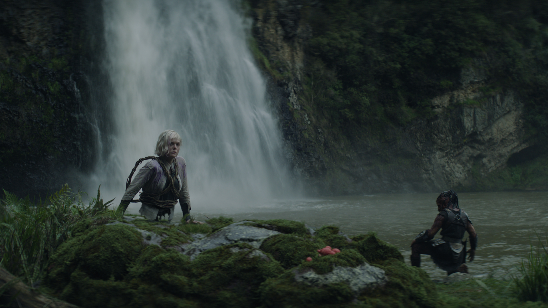 A still from Predator: Badlands featuring Thia (Elle Fanning) and Dek (Dimitrius Schuster-Koloamatangi) exploring near a waterfall