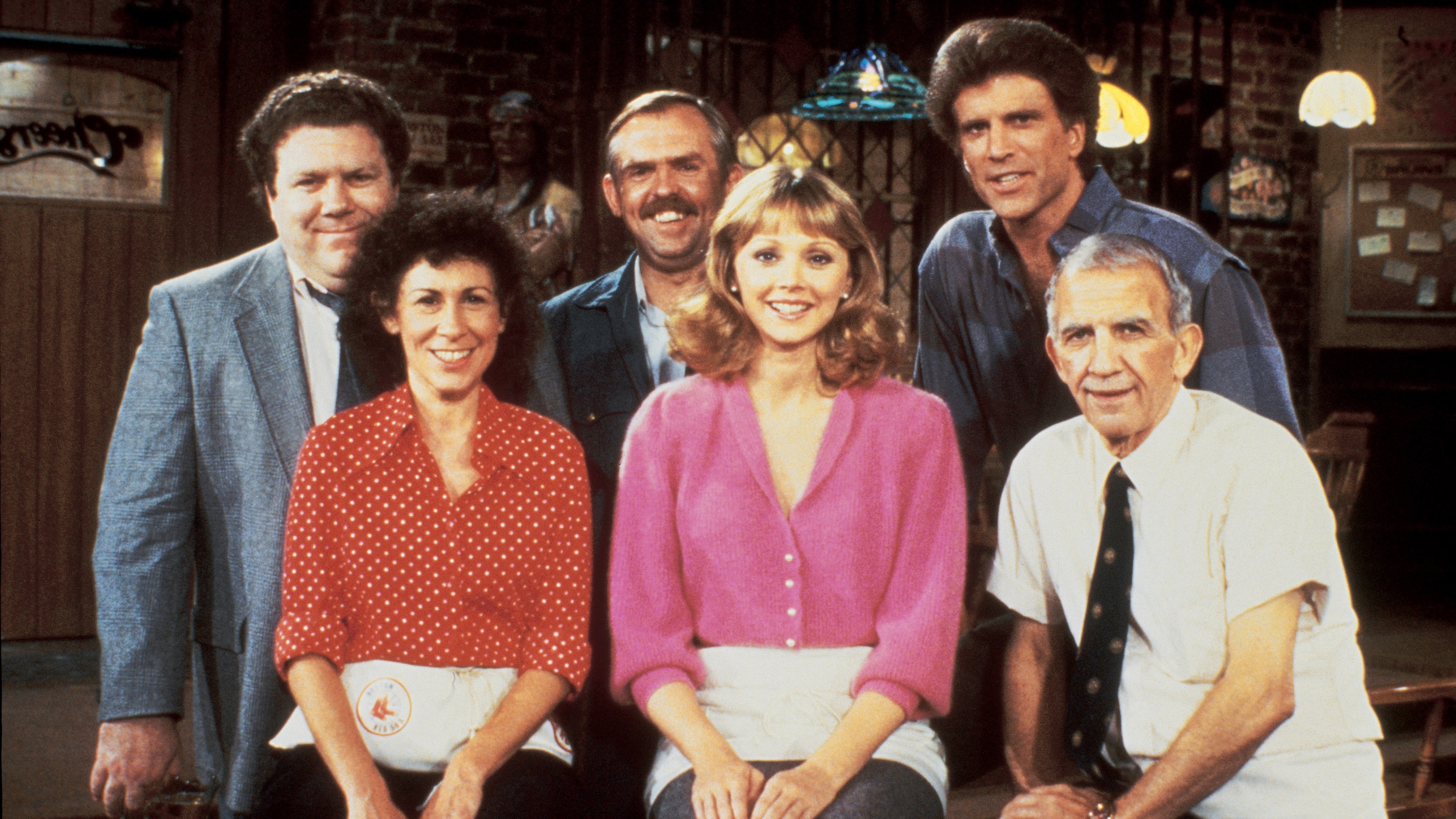 The cast of the 1980s sitcom Cheers posing together inside the show’s bar.