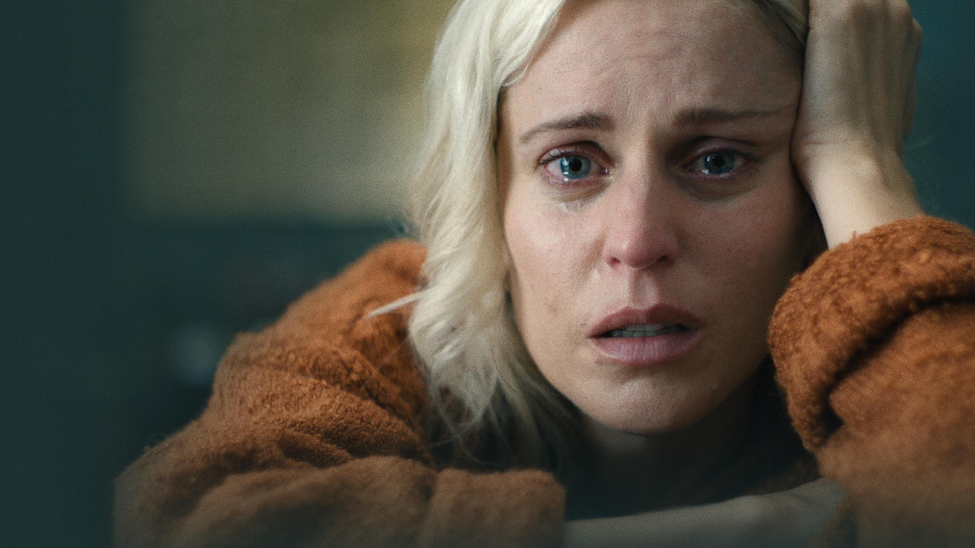 A close up of a woman with tears in her eyes, leaning her head against her hand