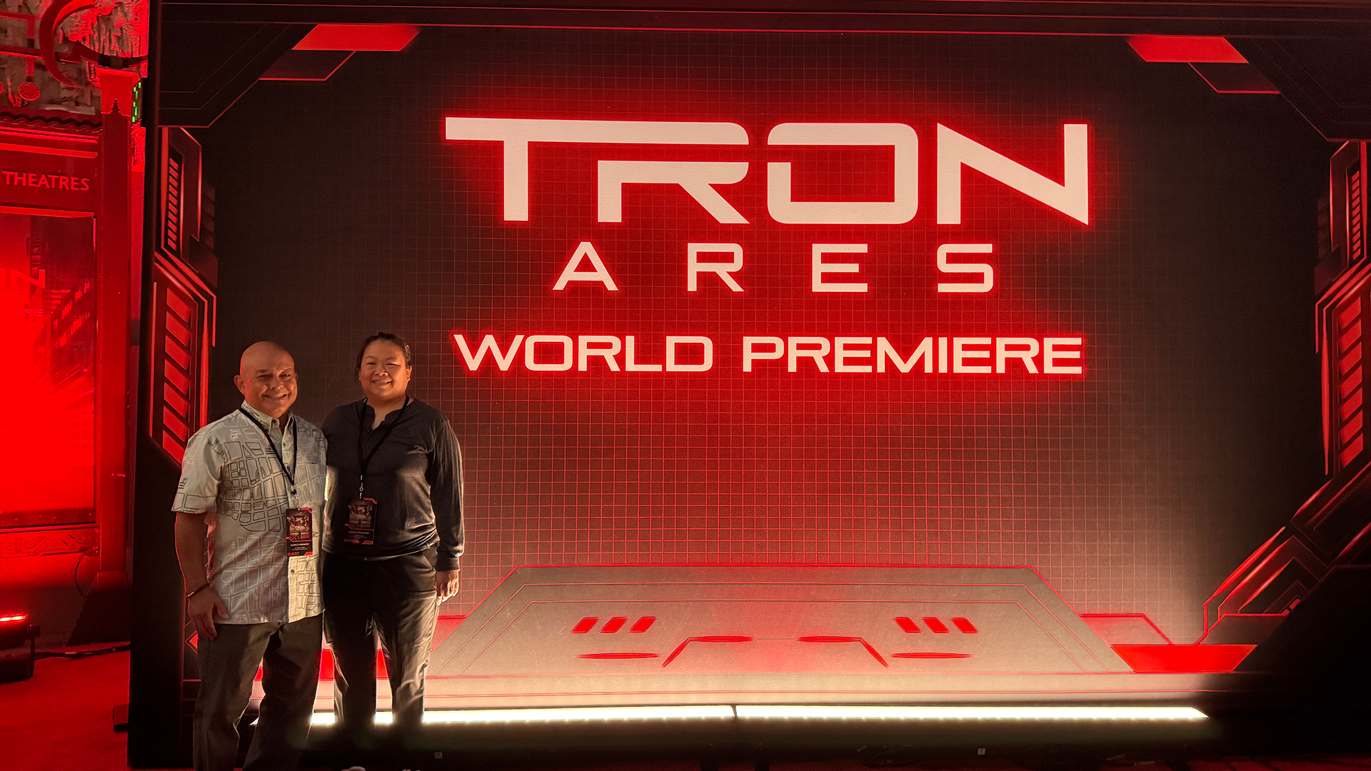Jeanine C. and her husband pose together with a futuristic red background reading "Tron: Ares World Premiere."