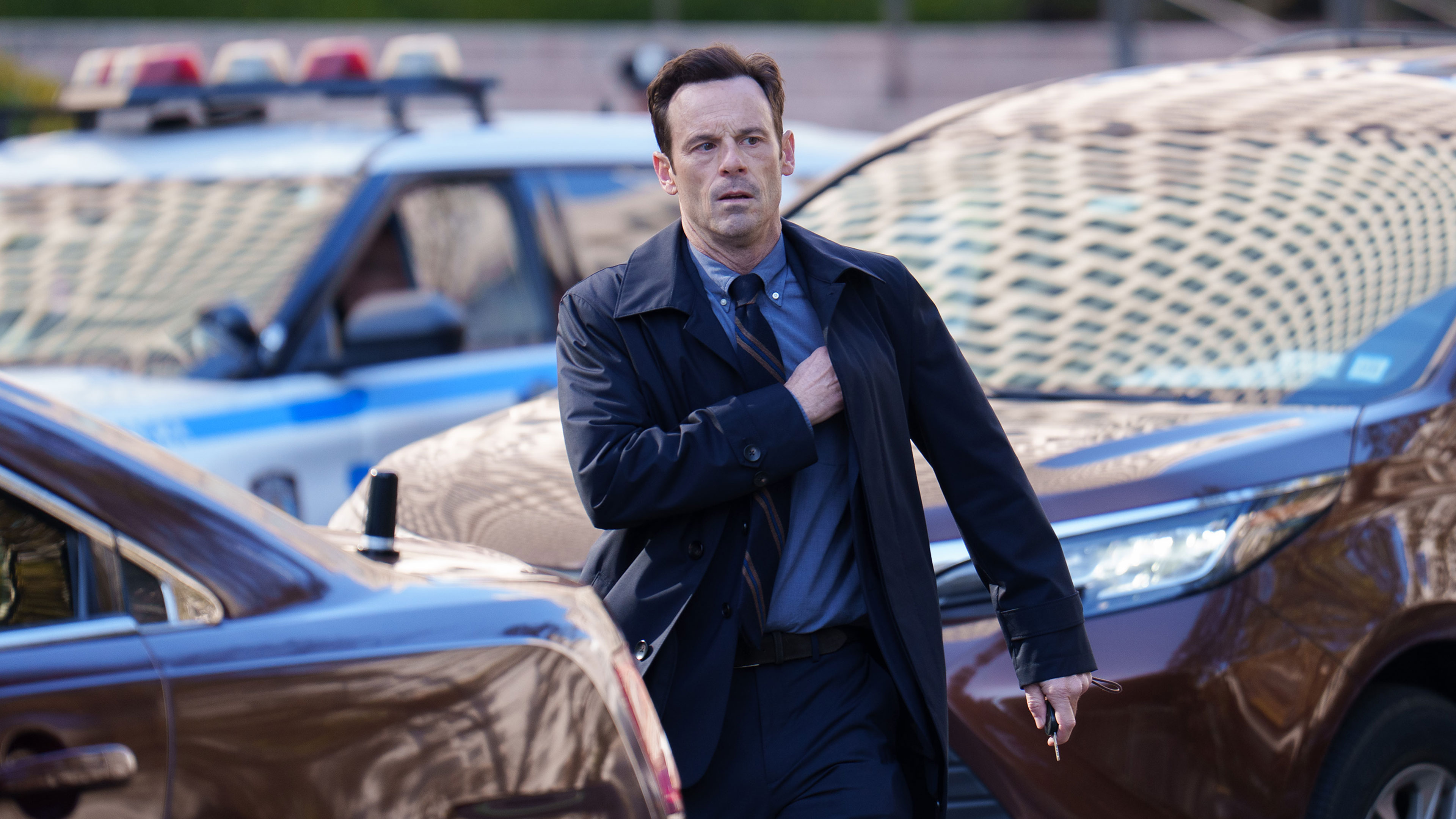Danny walks between parked vehicles near police cars.