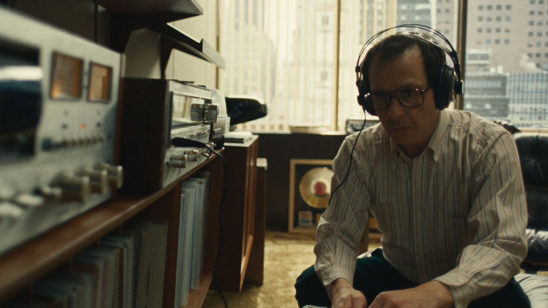 Jon Landau (Jeremy Strong), wearing headphones, listens to music on a record player.