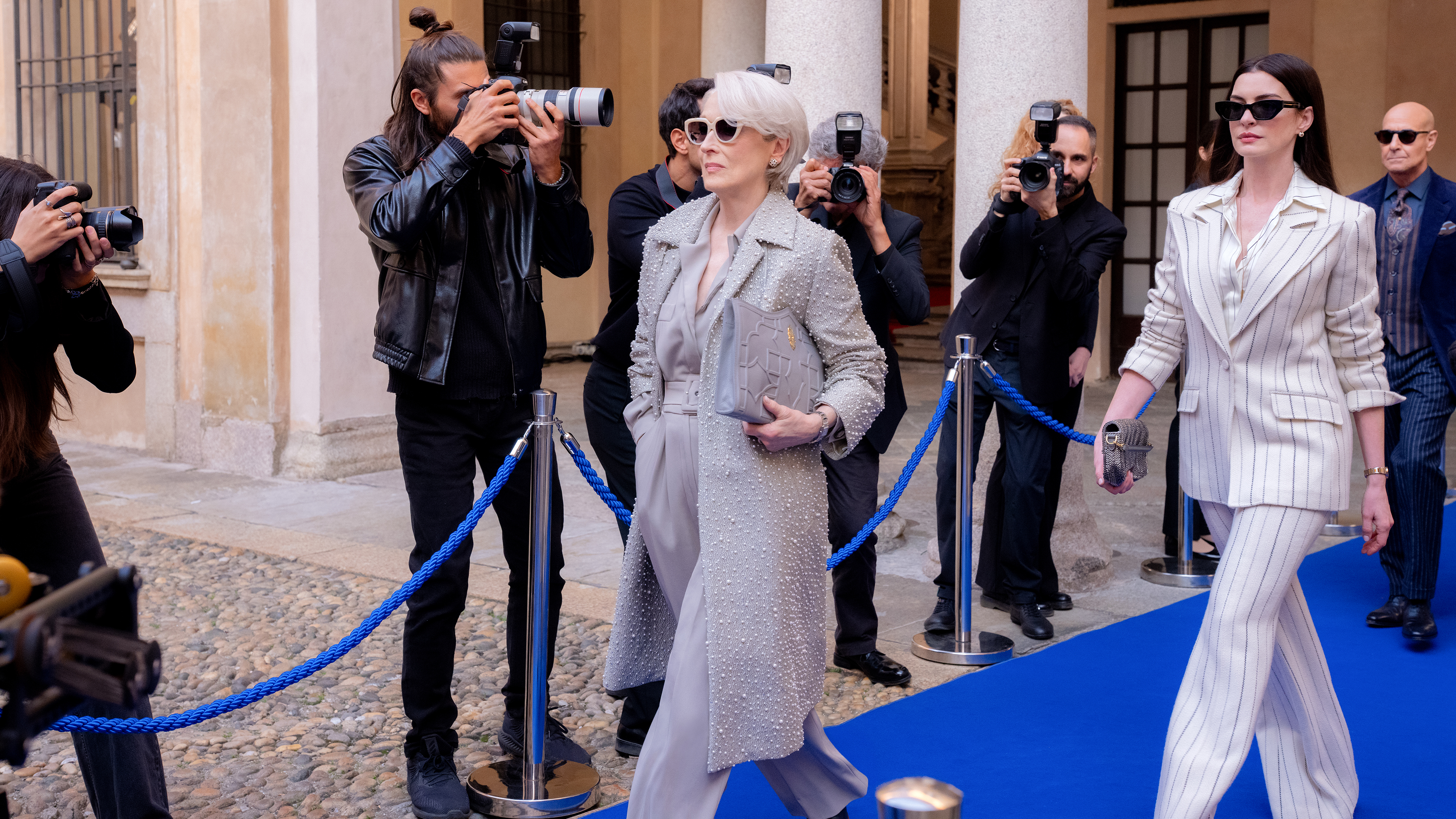 Miranda (Meryl Streep) and Andy (Anne Hathaway) walk down a blue carpet while paparazzi take photos of them in The Devil Wears Prada 2.