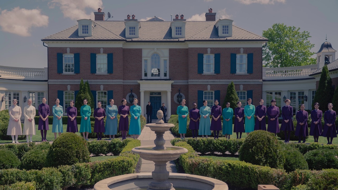 Women in color-coded uniforms stand in formation outside a large estate in Gilead, as seen in The Testaments on Hulu.