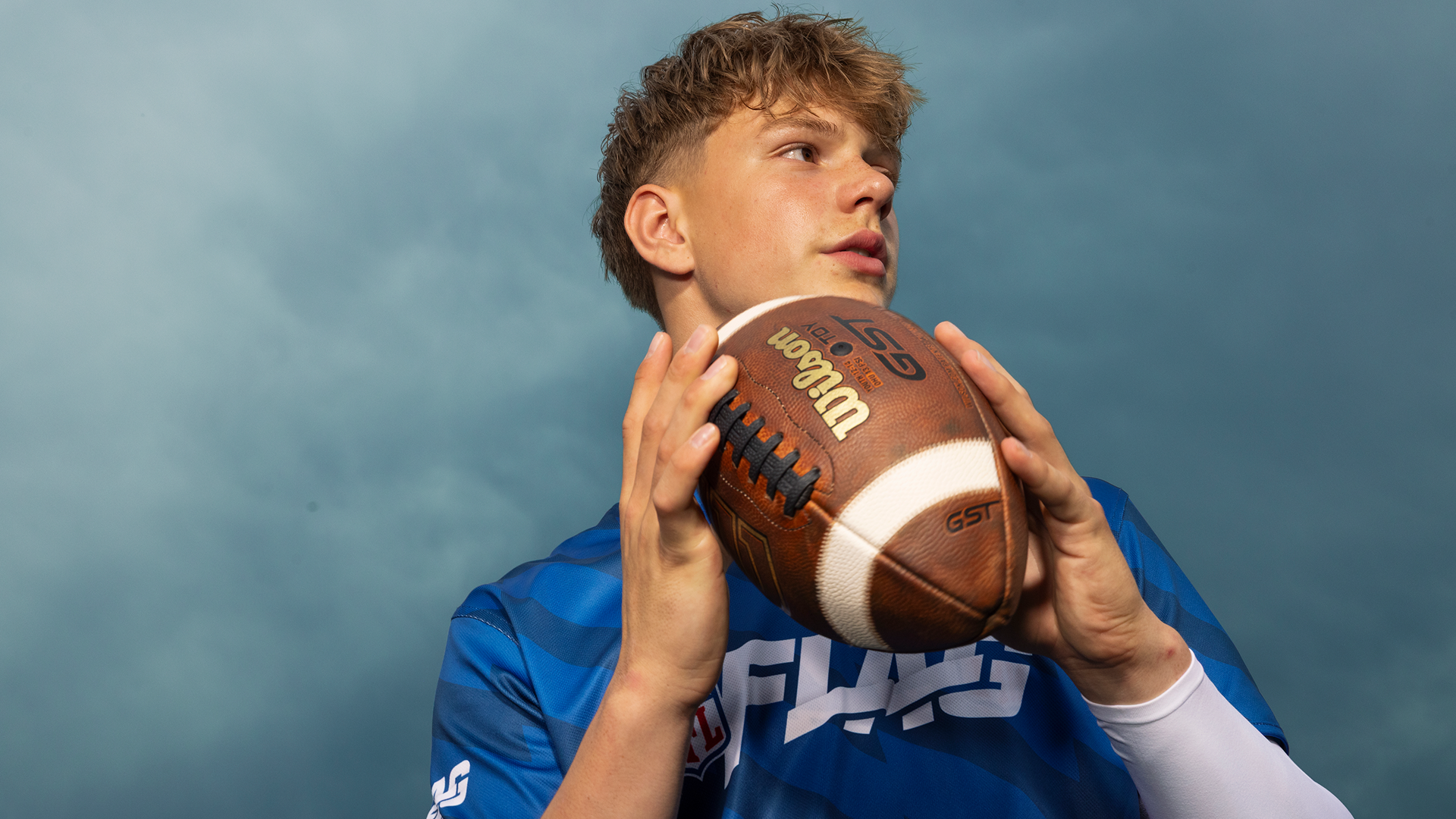 Close-up of a young man holding the football in both hands as he scans the field.