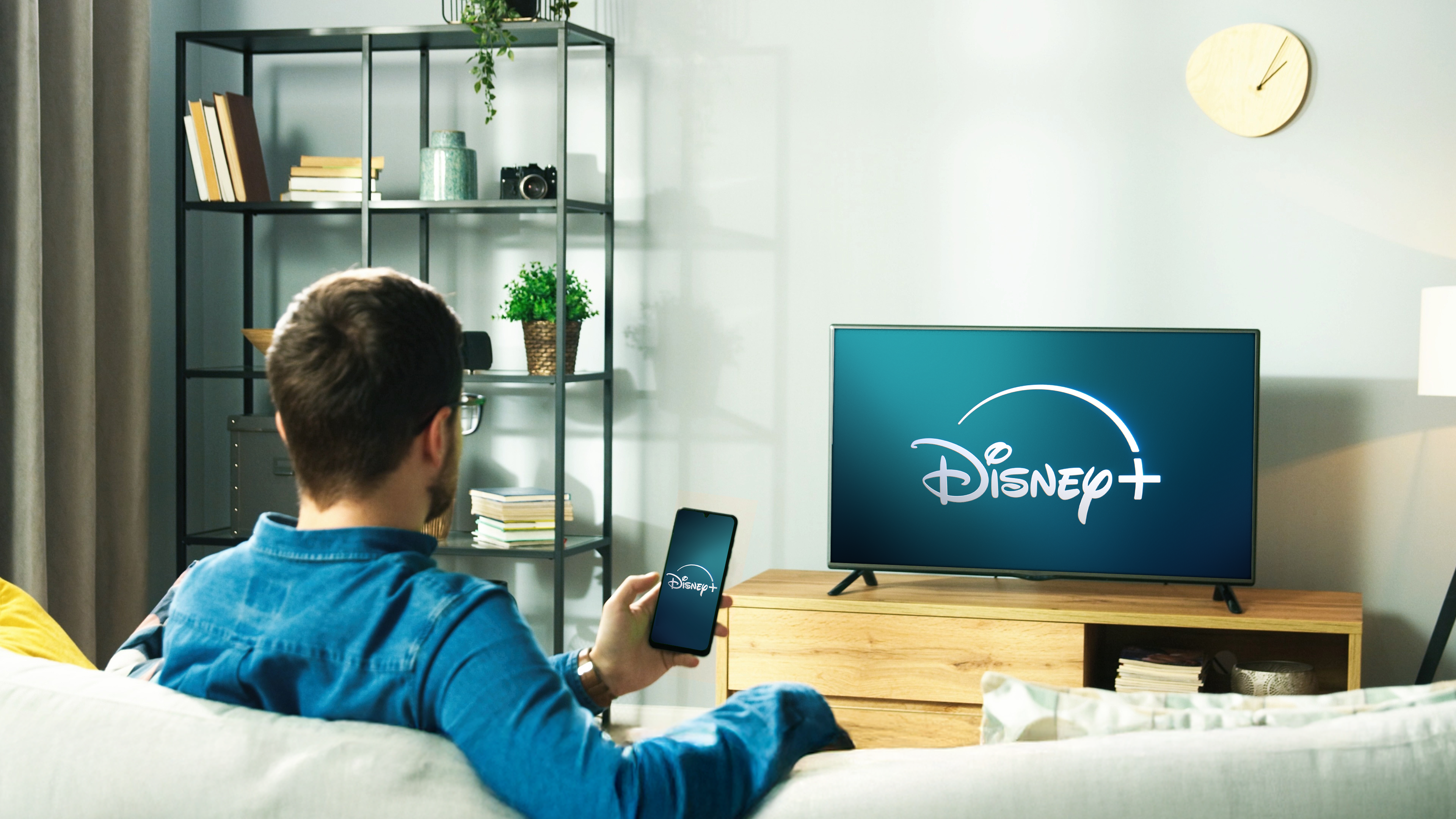 Man watching television in his living room, the television showcases the Disney+ start screen