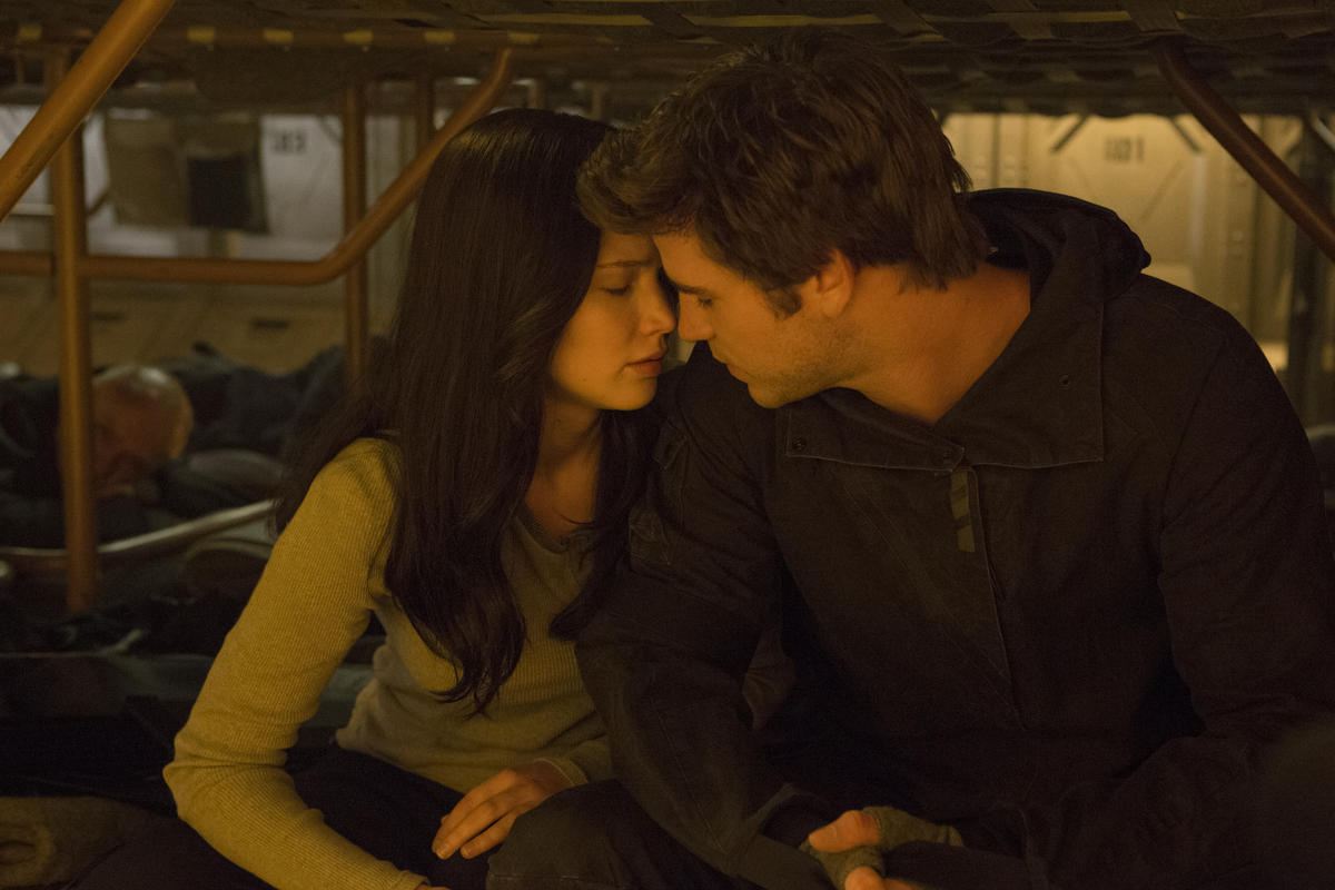 Liam Hemsworth as Gale Hawthorne leans in close with Jennifer Lawrence as Katniss Everdeen in a dimly lit scene from The Hunger Games saga.