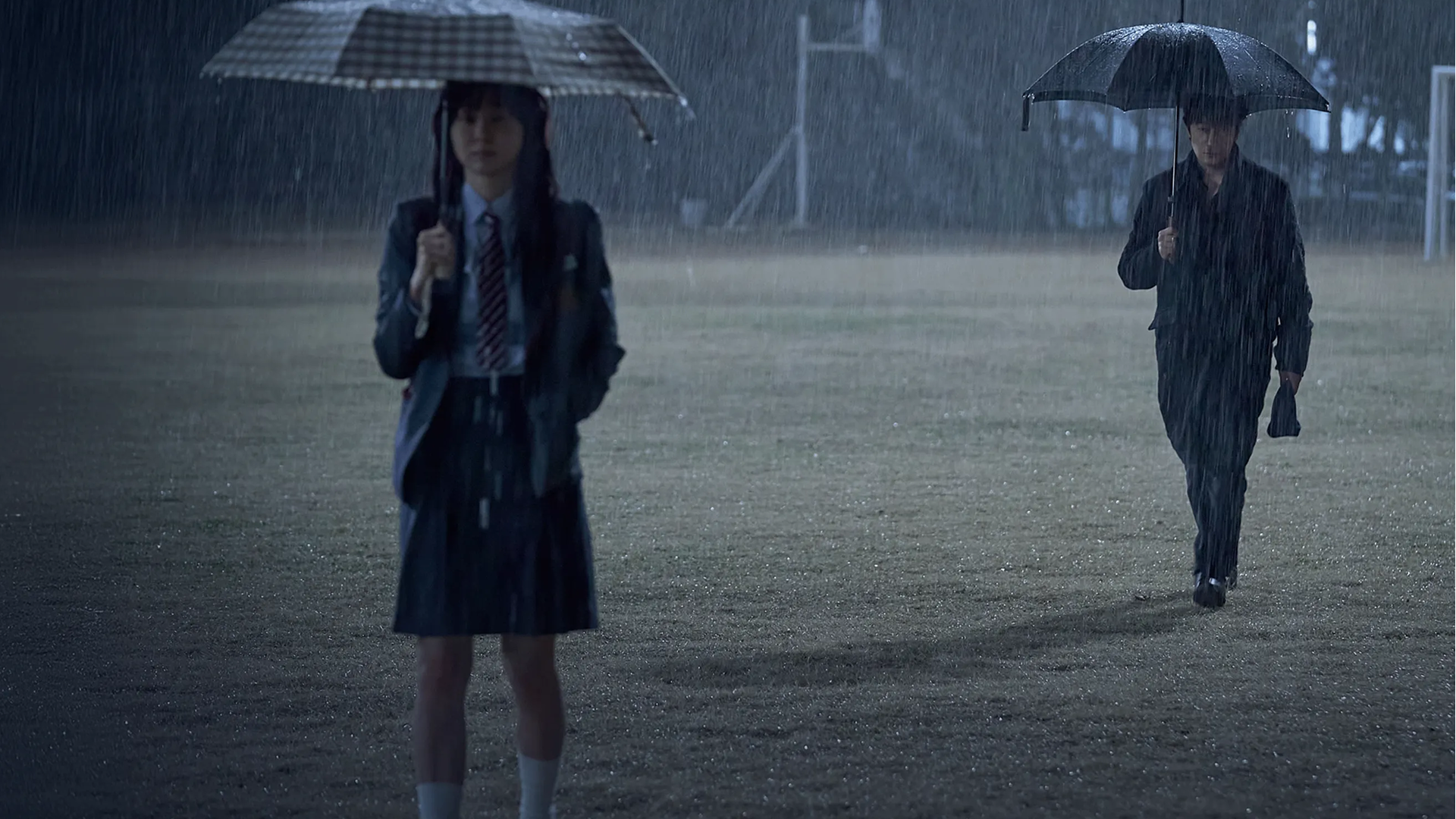 Os personagens principais de Nove Peças parados na chuva em um campo esportivo.