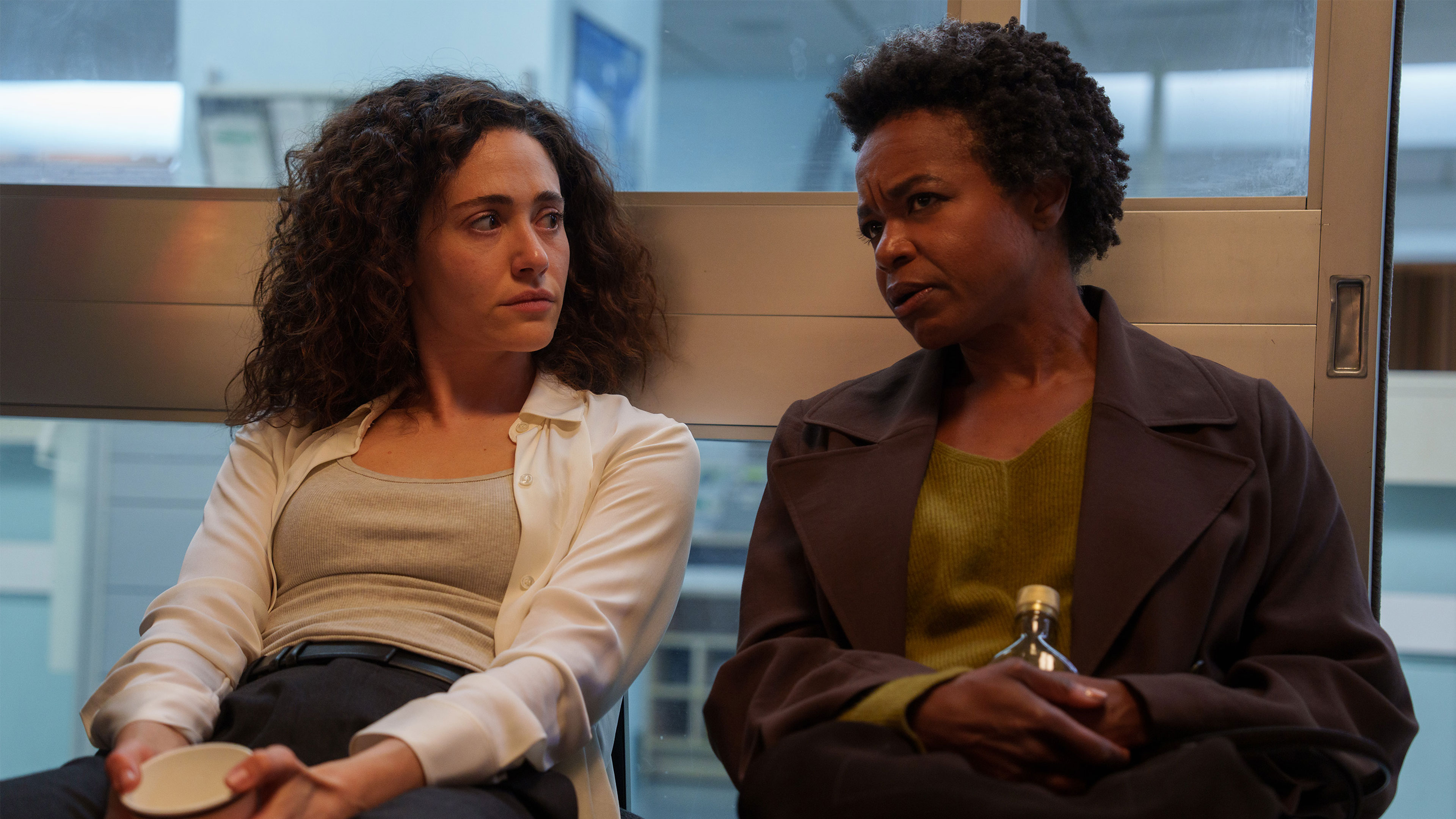 Alice and Nora sit together in a corridor talking.