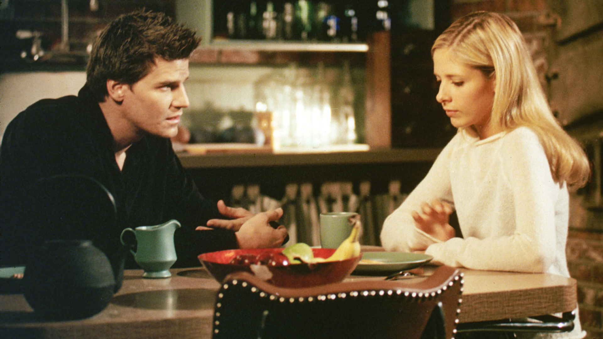 Buffy Summers (Sarah Michelle Gellar), sentada a la mesa de la cocina, habla con Angel (David Boreanaz) en el episodio cruzado de Angel "Te recordaré"